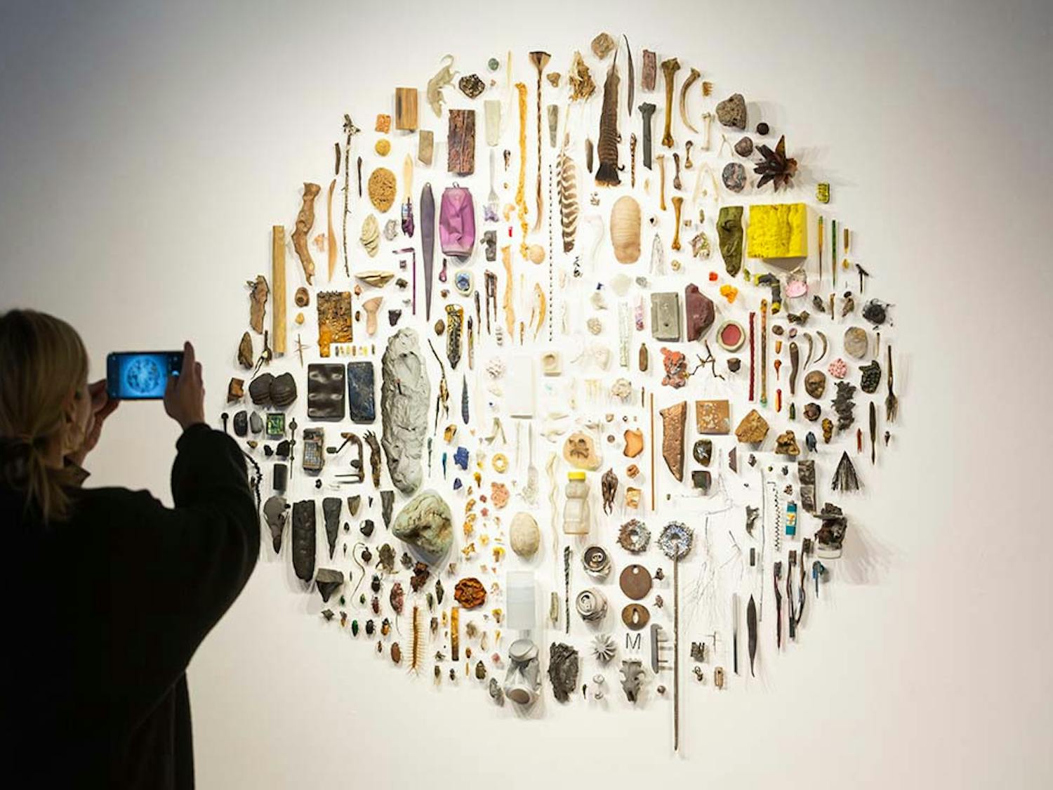 A visitor takes a photo of "Some Things" by Christopher Mahonski in the Voyage of Life exhibit featured in the McMaster Gallery. The sculpture is a collection of found and fabricated materials to explore the subject of ecological uncertainty.