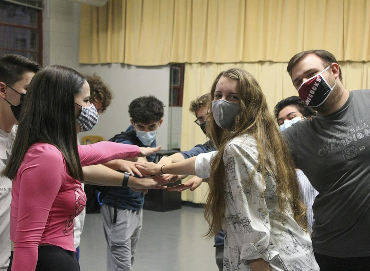 Members of the OverReactors Improv troupe form a hand stack in a circle as they smile at the camera.&nbsp;