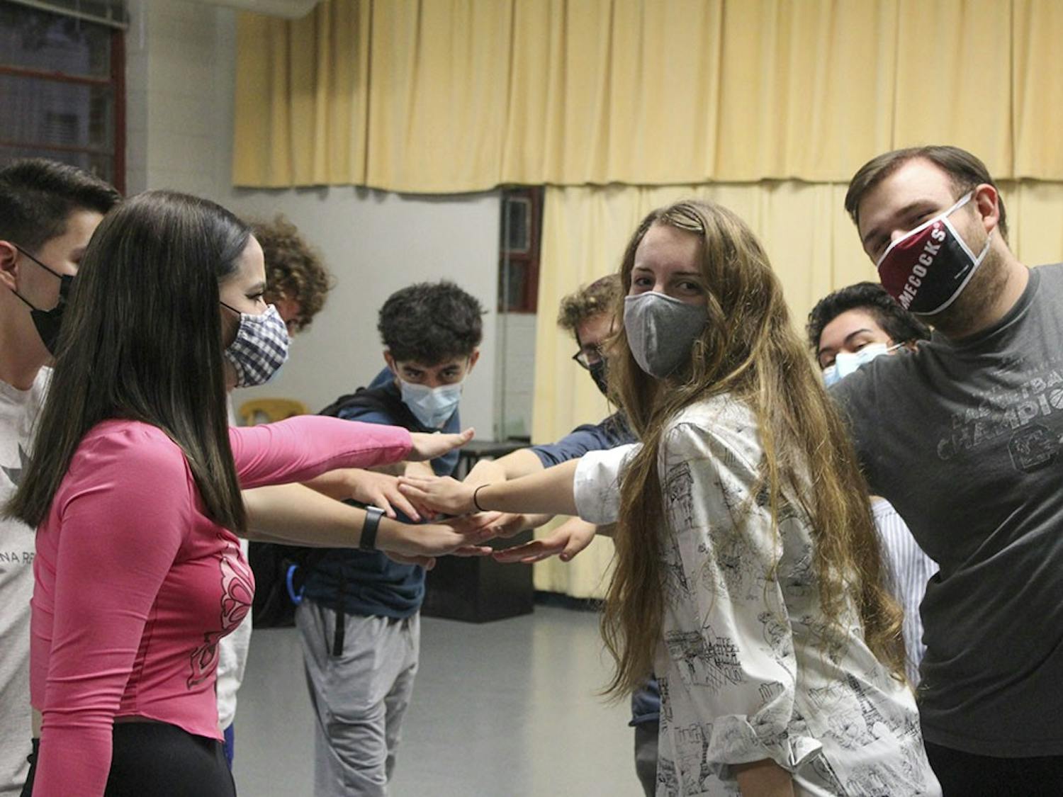Members of the OverReactors Improv troupe form a hand stack in a circle as they smile at the camera. 