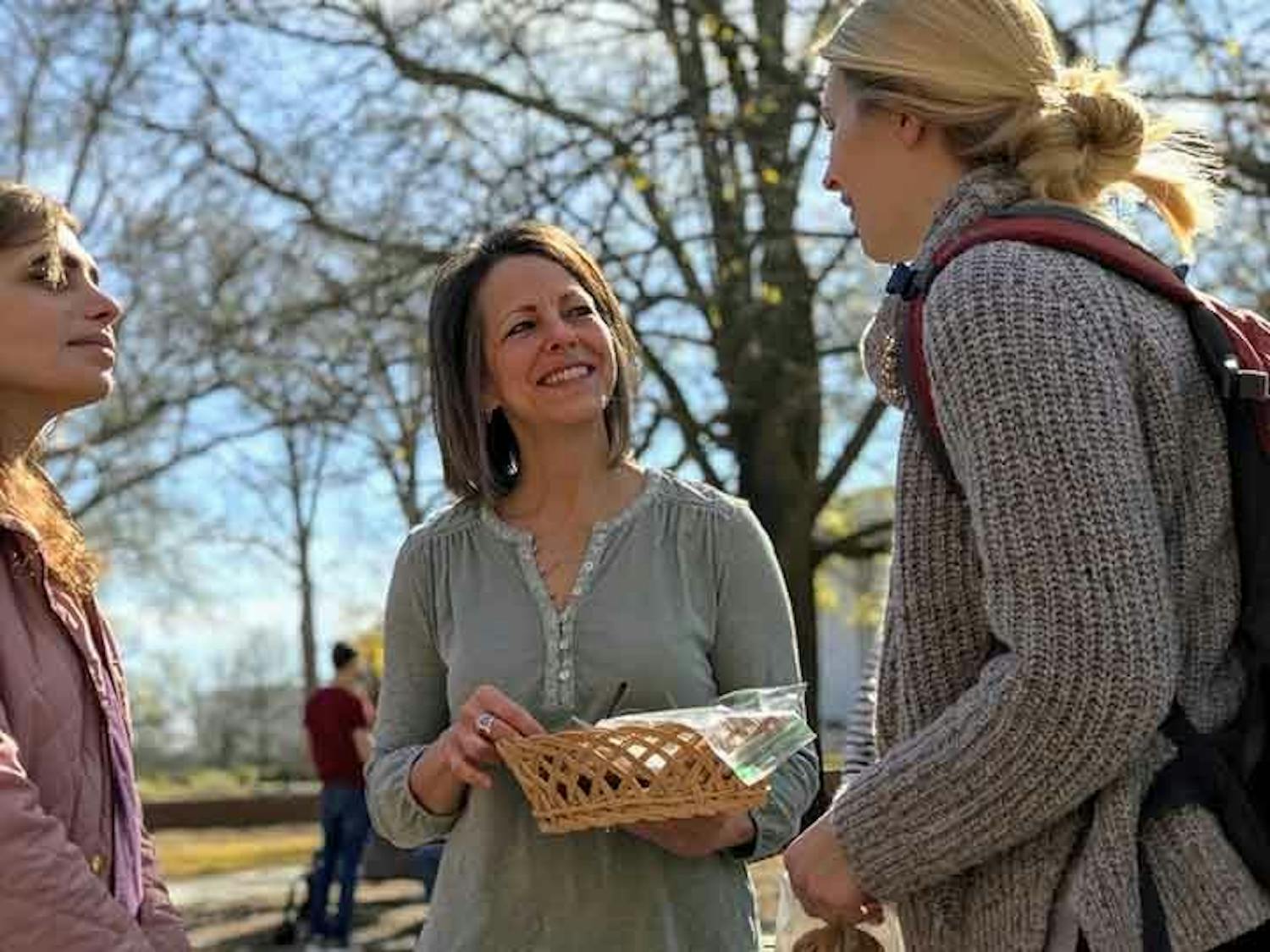 A student talks to an Ask a Mom member who holds a basket of cookies while in the clapping circle near Davis Field.
