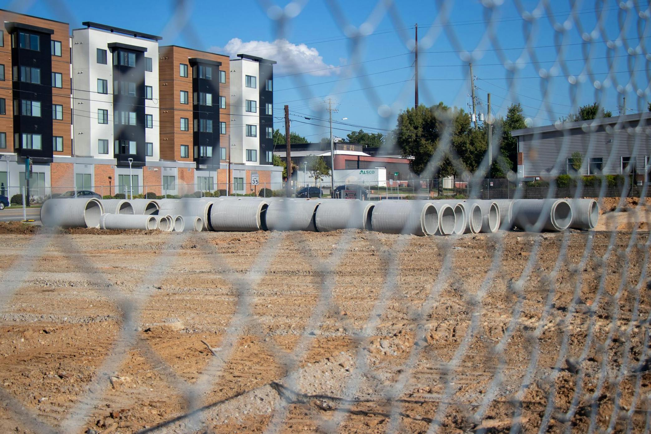 Rows of construction tubes lie in the dirt, with Park Place in the background and a fence out of focus in the foreground.