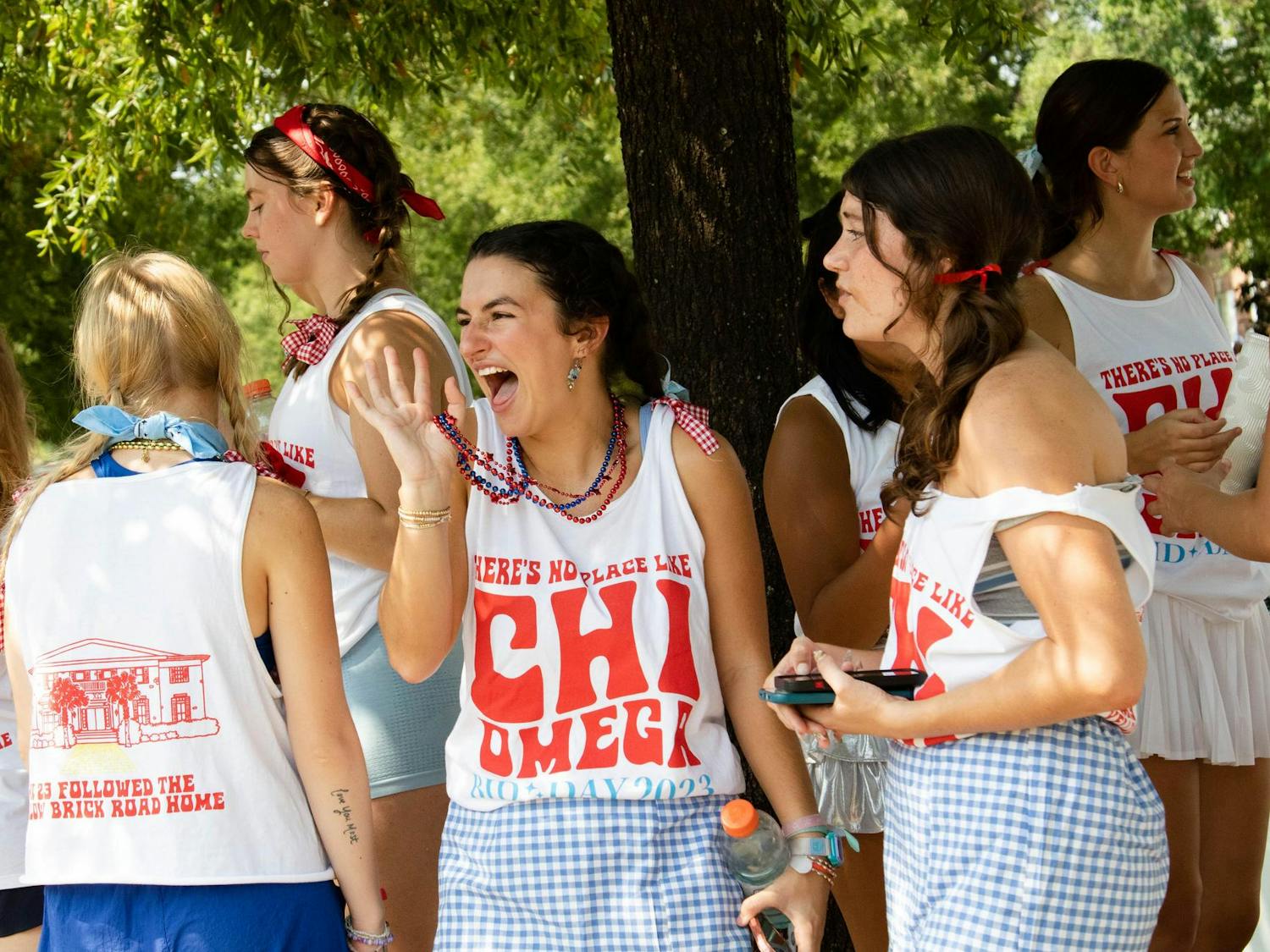 Chi Omega sisters wear shirts saying "There's no place like Chi Omega" while cooling off under a tree during Bid Day. The sisters spent time outside, celebrating their new members in temperatures over 90 degrees.