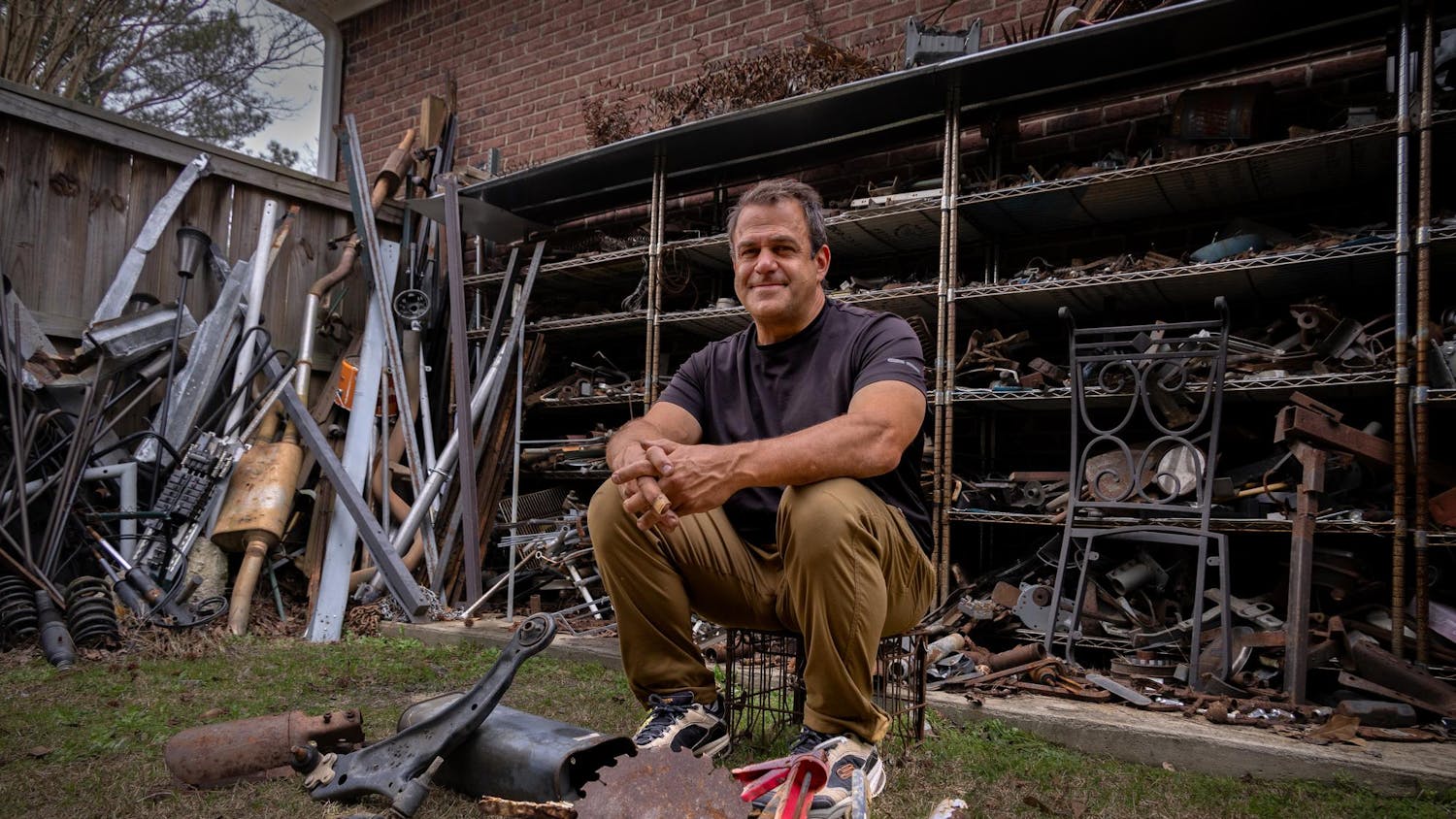 Humphries, who is also a business owner, poses for a photo in his outdoor workshop in West Columbia on Feb. 27, 2024. Humphries' shelves contain only some of the materials that he uses to create sculptures.