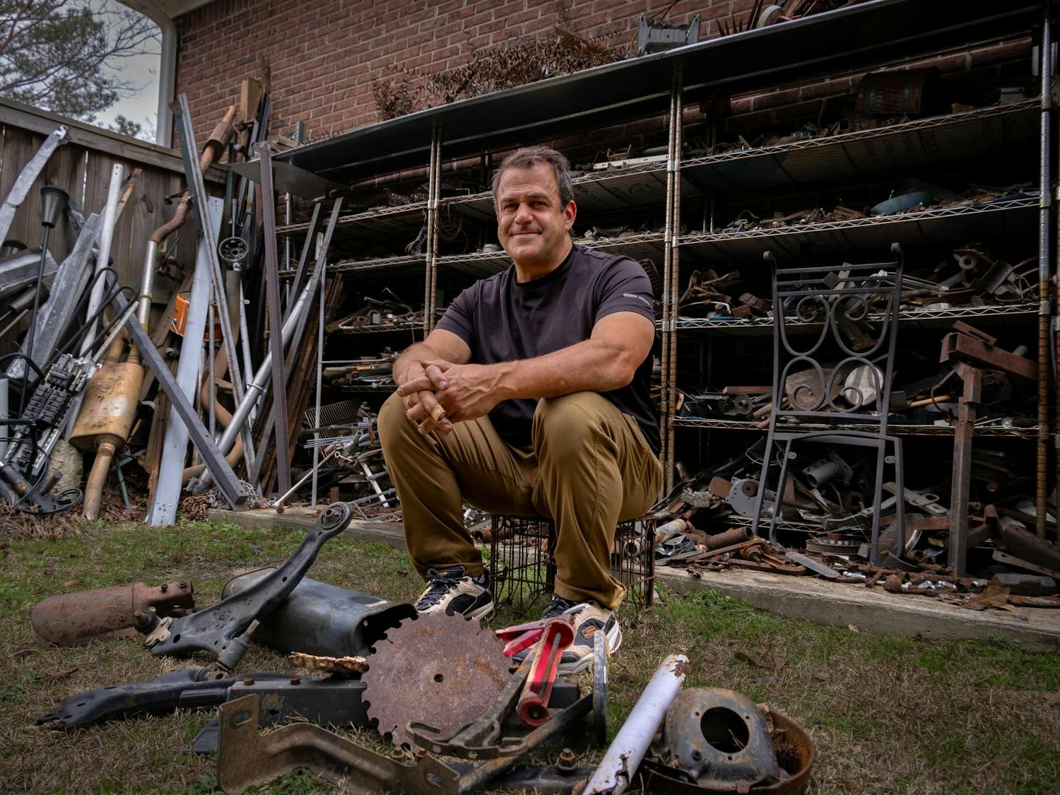 Humphries, who is also a business owner, poses for a photo in his outdoor workshop in West Columbia on Feb. 27, 2024. Humphries' shelves contain only some of the materials that he uses to create sculptures.