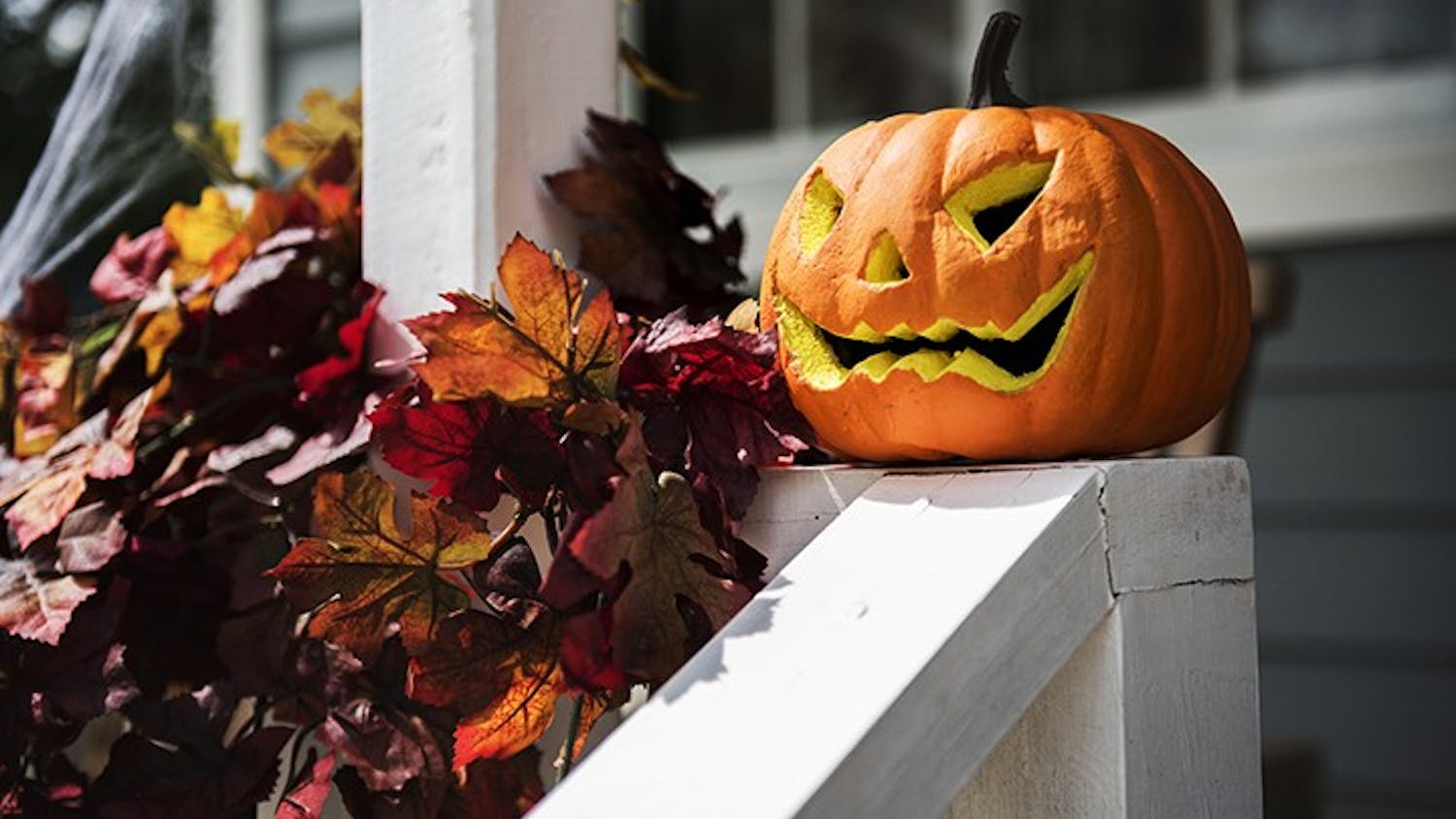 A jack-o'-lantern sits on top of a railing. Carving pumpkins into jack-o'-lanterns is often a popular fall activity.