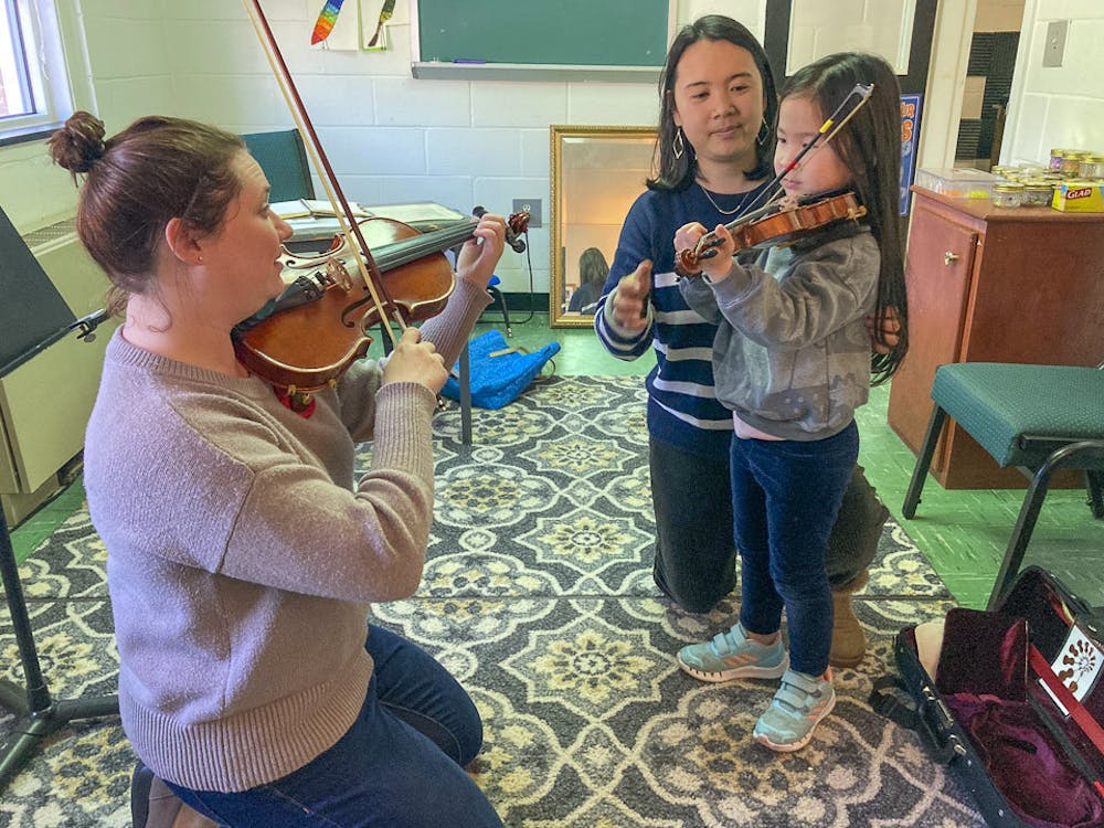 <p>Violinist Jessica Rafferty (left) teaches a violin lesson to a student (right), as her mother helps her. The Suzuki Academy is a non-profit organization that teaches children how to play music from a young age.</p>