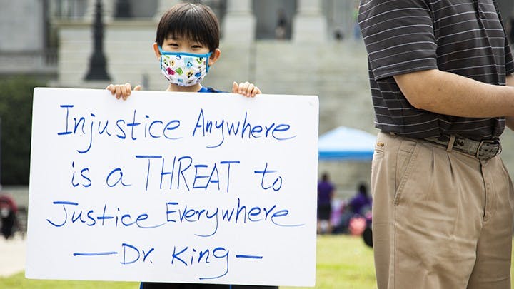 A young child holds a sign that says “Injustice Anywhere is a THREAT to JusticeEverywhere -Dr. King” during a protest about stopping Asian hate in America.

