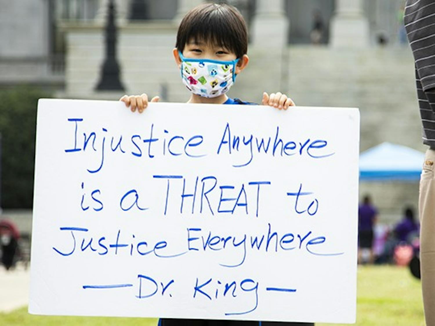 A young child holds a sign that says “Injustice Anywhere is a THREAT to JusticeEverywhere -Dr. King” during a protest about stopping Asian hate in America.
