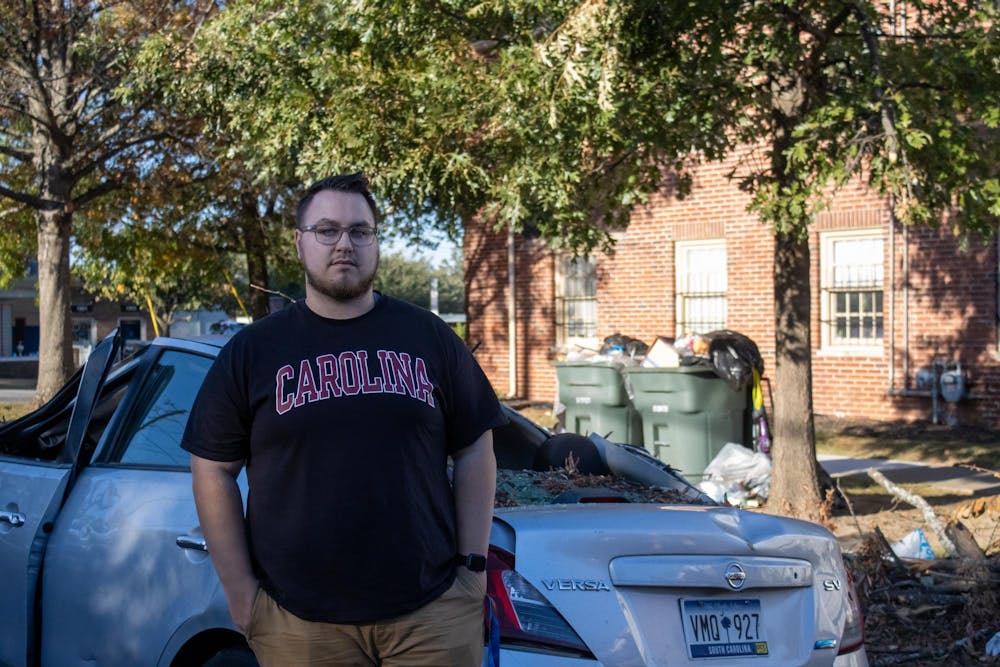 <p>FILE—Graduate student Matthew Snyder stands in front of an abandoned car left outside his apartment by a neighbor on Oct. 23, 2024. The car was totaled after a tree fell directly on top of it during Hurricane Helene.</p>