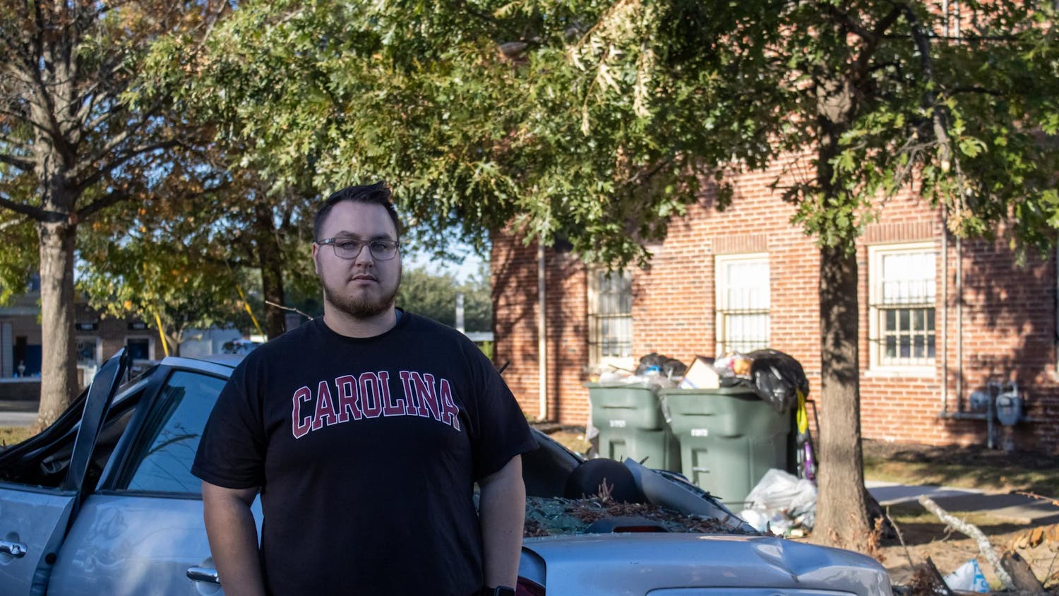 FILE—Graduate student Matthew Snyder stands in front of an abandoned car left outside his apartment by a neighbor on Oct. 23, 2024. The car was totaled after a tree fell directly on top of it during Hurricane Helene.