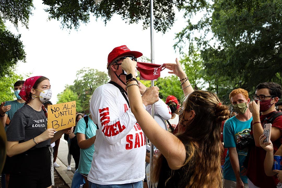 A student holds up a University of South Carolina face mask in attempt to cover Jim Gilles' “MAGA Fire Fauci” facemask. Jim Gilles took off his mask soon after.
