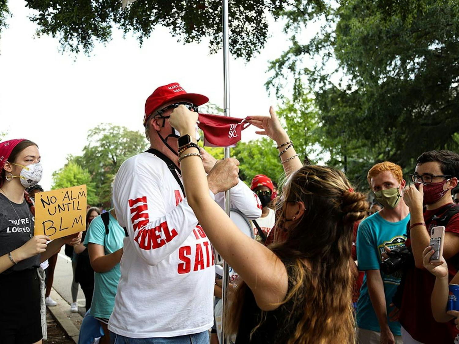 A student holds up a University of South Carolina face mask in attempt to cover Jim Gilles' “MAGA Fire Fauci” facemask. Jim Gilles took off his mask soon after.