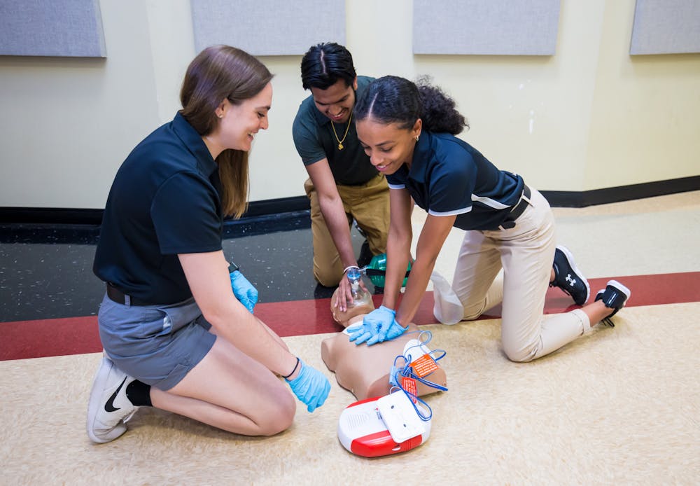 <p>Three students practice CPR and AED application on a manikin. CPR and AED are necessary procedures for athletic trainers to learn in order to know how to respond in an emergency situation.&nbsp;</p>