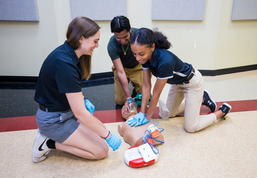 <p>Three students practice CPR and AED application on a manikin. CPR and AED are necessary procedures for athletic trainers to learn in order to know how to respond in an emergency situation. </p>