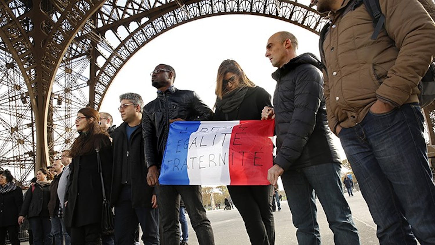 Paris residents take part in a moment of silence under the Eiffel Tower on Monday, Nov.16, in observance of those who died during the terrorist attacks three days ago. Holding a French flag with the words &quot;Liberty, Equality, Brotherhood,&quot; participants stand united during a minute of silence. (Carolyn Cole/Los Angeles Times/TNS)