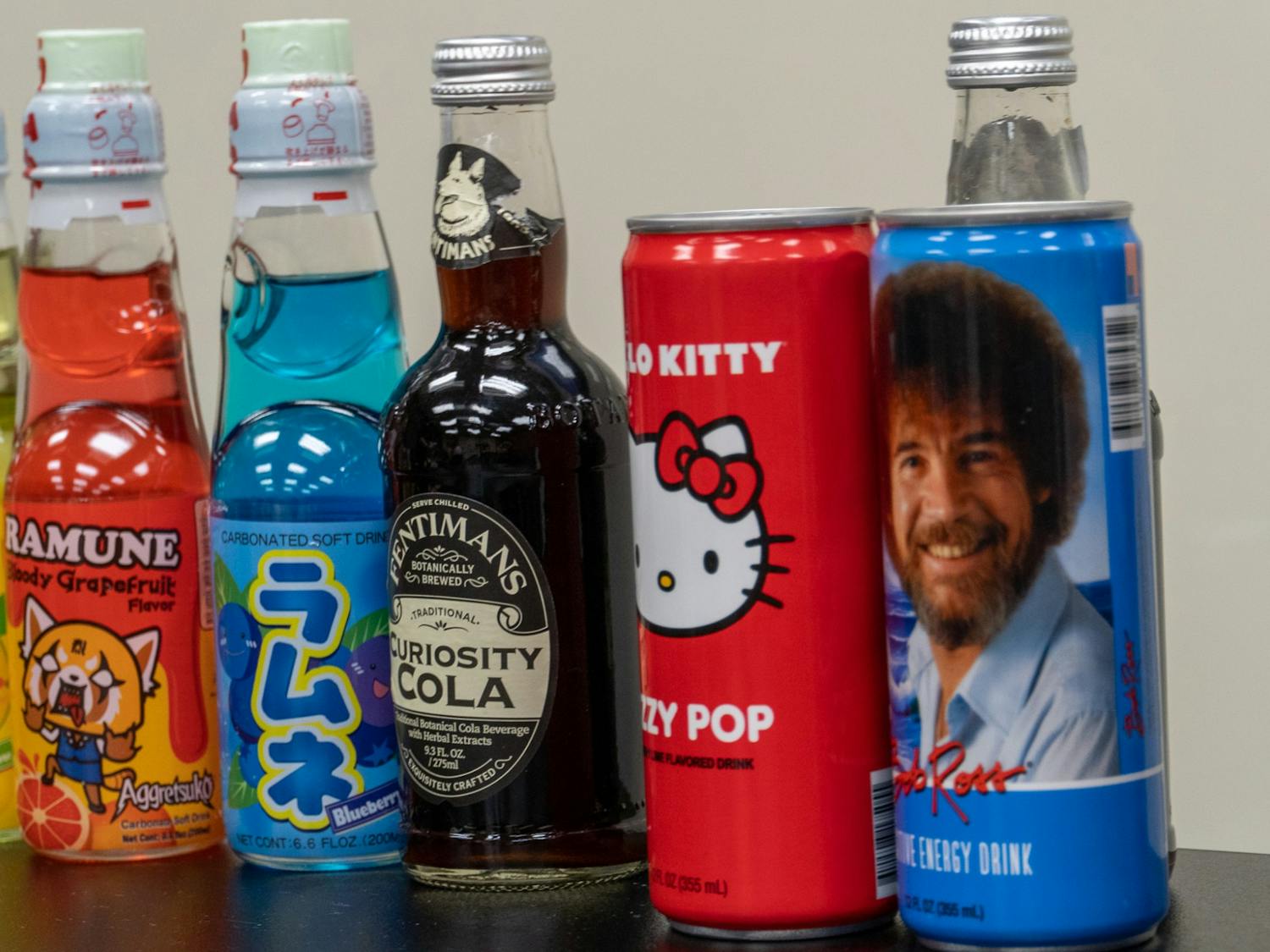 An assortment of drinks sampled during a club meeting centered around trying a unique variety of sodas including Curiosity Cola, Bob Ross brand energy drinks and many other beverages. 
