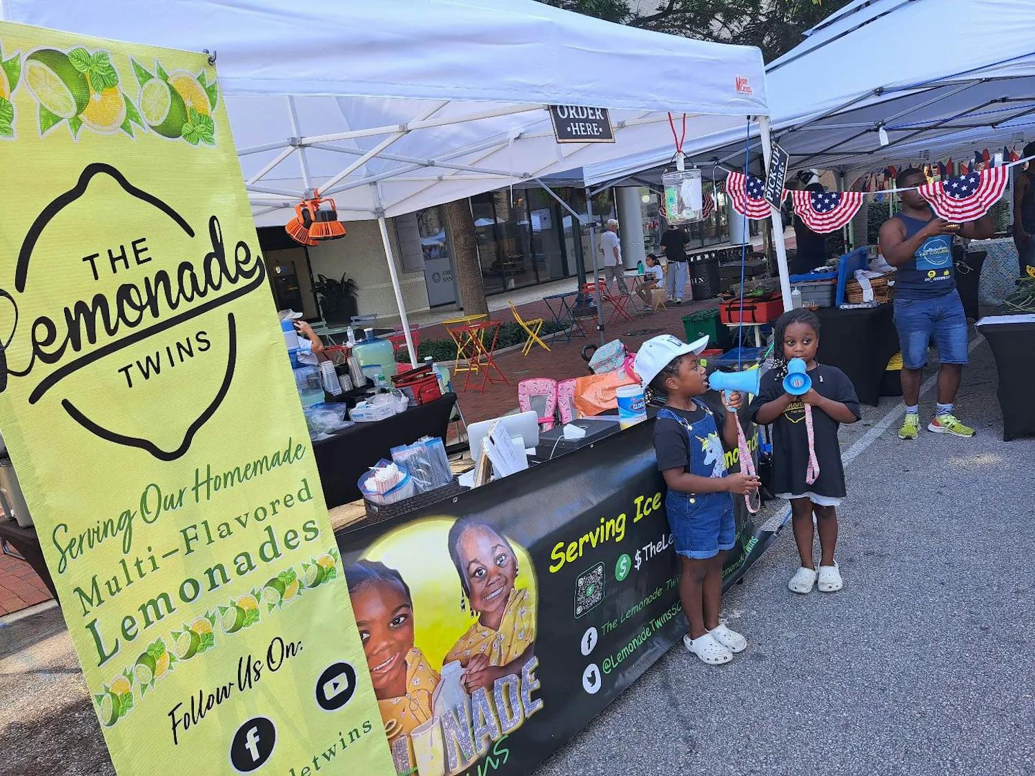 The Lemonade Twins, Faith and Malia Jeffcoat, pictured announcing the sale of their lemonade at the Soda City market on a Saturday morning in Columbia, South Carolina. The dynamic duo has been selling lemonade since June 2020 and have a variety of flavors to choose from.&nbsp;