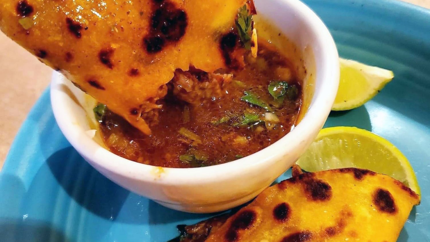 Birria tacos are dipped into consomme, the broth used to make the tortillas crispy and give color, at Real Mexico Restaurant in Columbia, SC. A side of consomme is always served with birria tacos, and it's customary to dip the tacos before every bite.