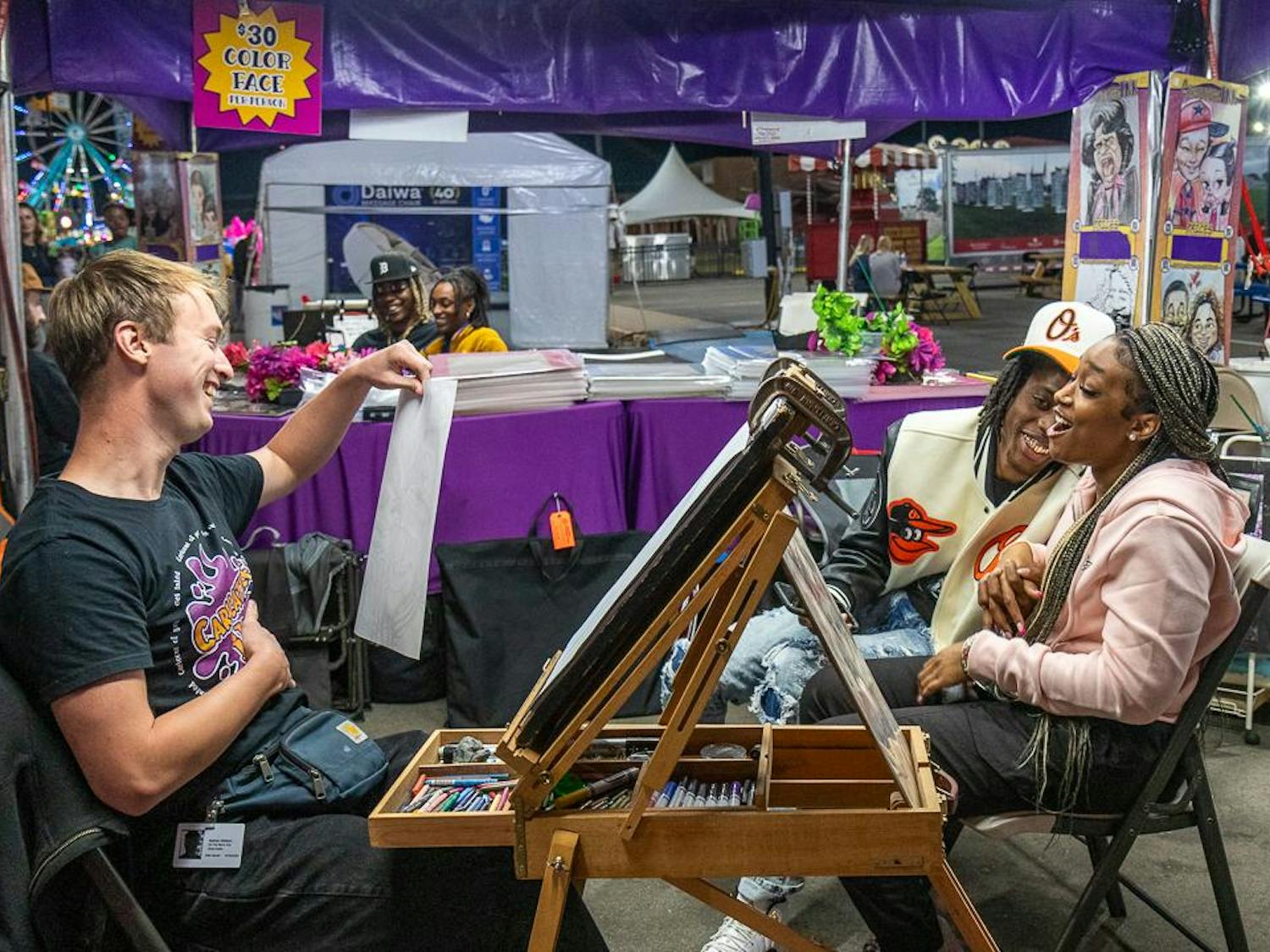 Azjour Jordan and Ralph Mitchell (right) laugh after caricature artist Nate Watson (left) presents their portrait at the South Carolina State Fair on Oct. 18, 2023. Watson, who is originally from Michigan, has been a caricature artist for four years and has been touring with the fair for one year.