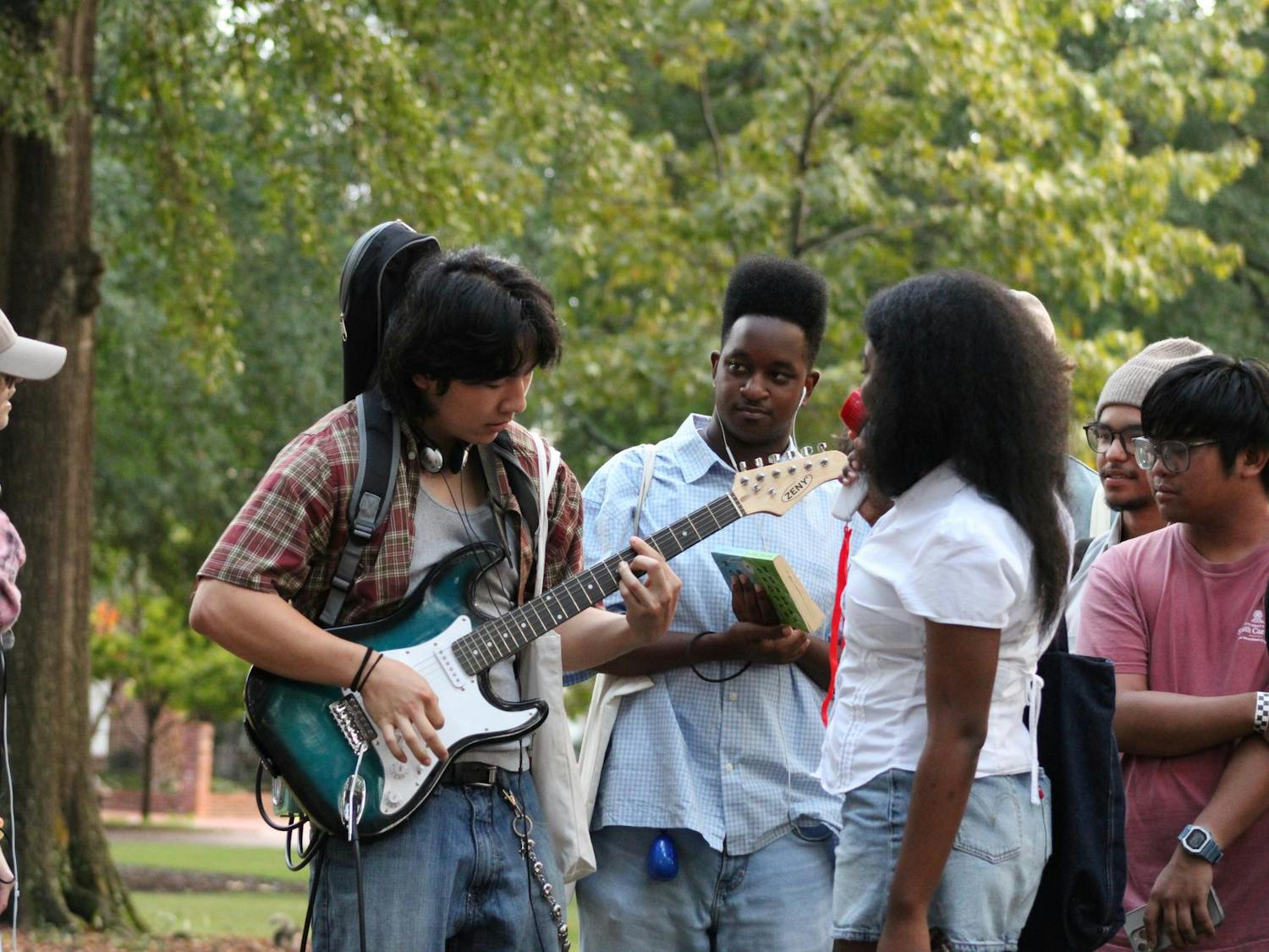 One of the contestants in the Performative Male Contest plays a song by Laufey on his electric guitar. The audience and his fellow contestants sing along as he plays.