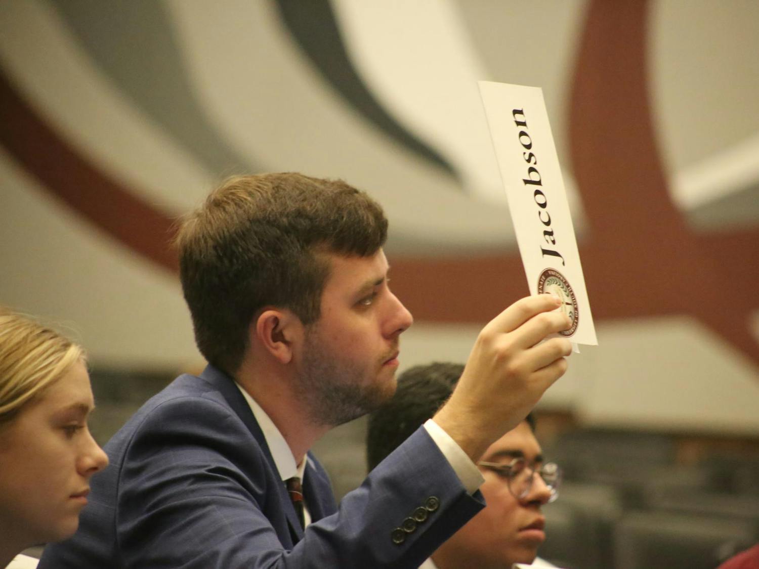 Student Government Senator Ash Jacobson raises his name card to ask a question during the Contested Second Reading Calendar period at the Russell House Auditorium on Nov. 5, 2025. Senators were given a chance to ask questions after a legislation was discussed during this time.
