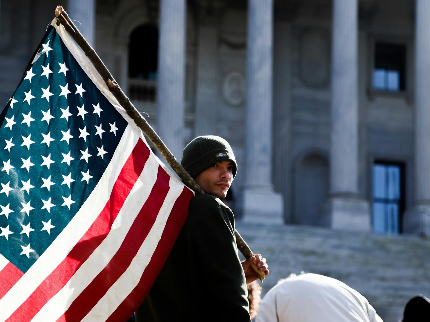 An attendee of the “Drive4America” caravan holds an American flag across his shoulder in front of the South Carolina Statehouse.&nbsp;