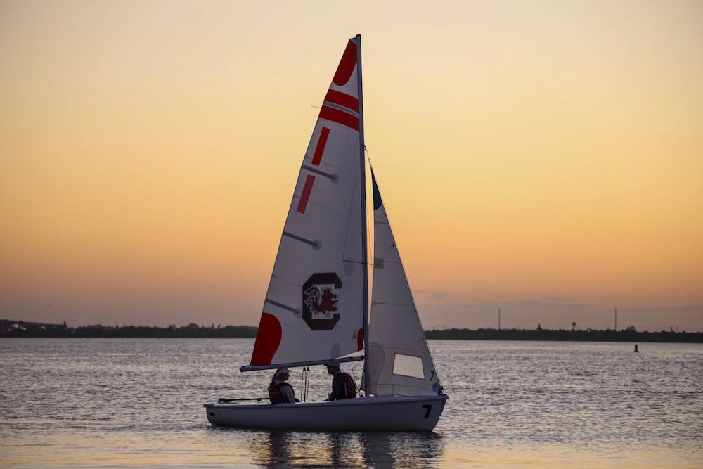 Two members of the sailing club sit on one of the sailboats during a sunset.