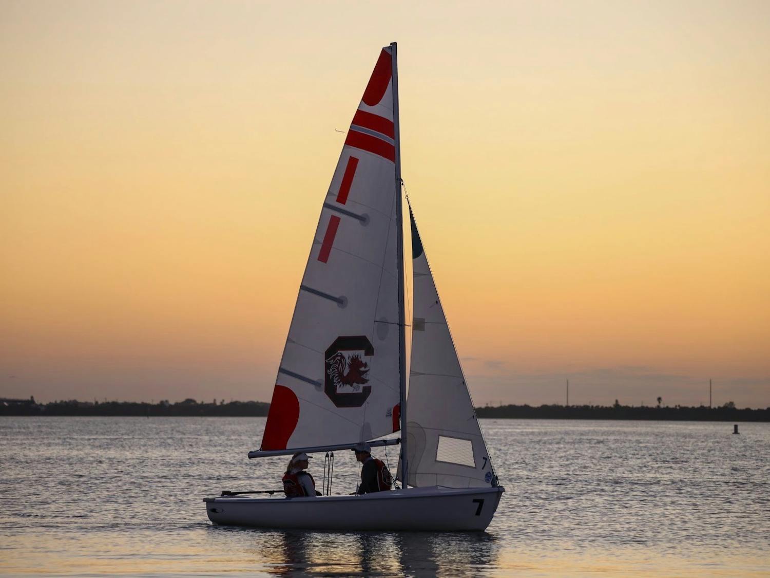 Two members of the sailing club sit on one of the sailboats during a sunset.