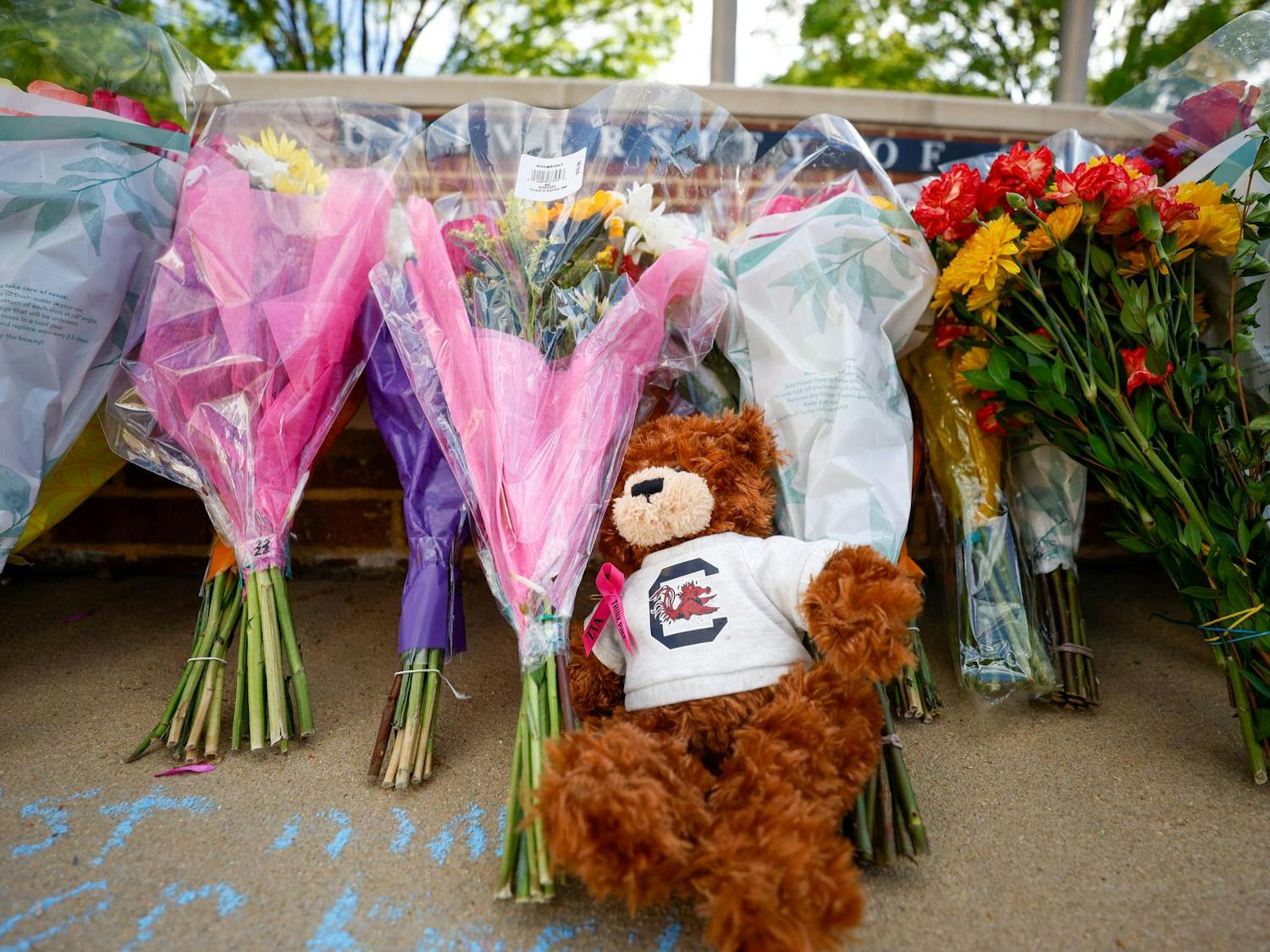 A teddy bear wearing a USC shirt sits in front of a line of flowers at a memorial honoring Nathaniel "Nate" Baker at Strom Thurmond Wellness and Fitness Center on April 3, 2025. Students and faculty left flowers and other memorabilia in memory of Baker who died the previous day.