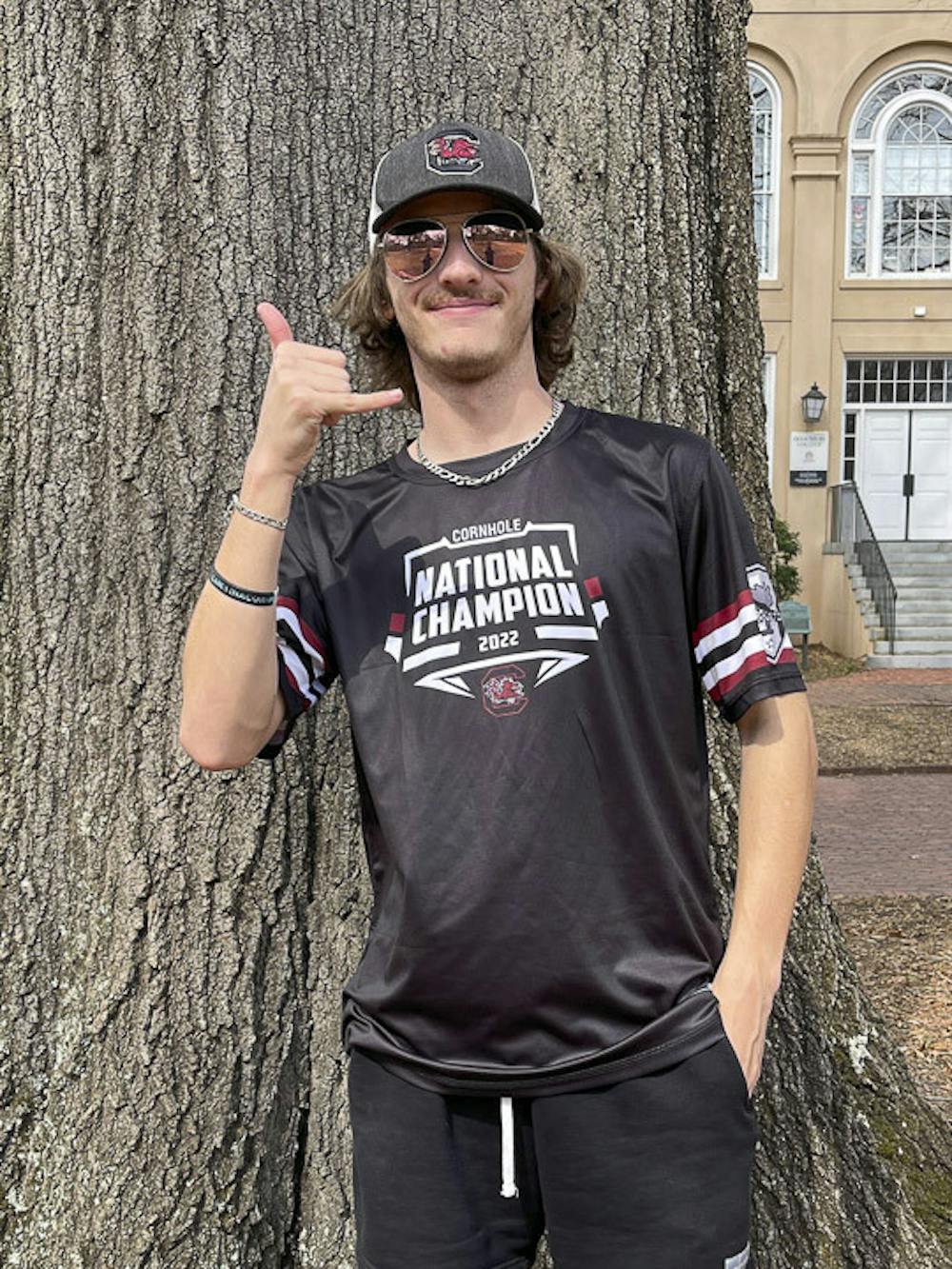<p>First-year sport and entertainment management student Nolan Cochran poses on the Horseshoe wearing a t-shirt commemorating South Carolina’s national championship in cornhole on Feb. 23, 2023. Jo Nathan, a fellow participant in a local cornhole league, provided these shirts to the team.</p>