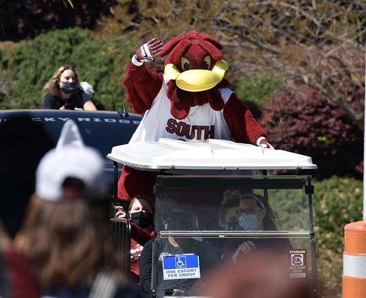 A golf cart leads the procession of Gamecock women's basketball players, with Cocky waving at the team's fans from the back of it.