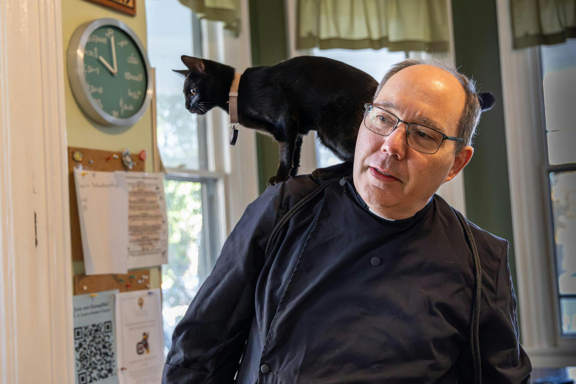Father Paul Sterne looks out the window while Lucy II stands on his shoulders at the C.S. Lewis Student Center on Nov. 10, 2025. Father Sterne is the primary caretaker of the four cats that roam the area near the center.
