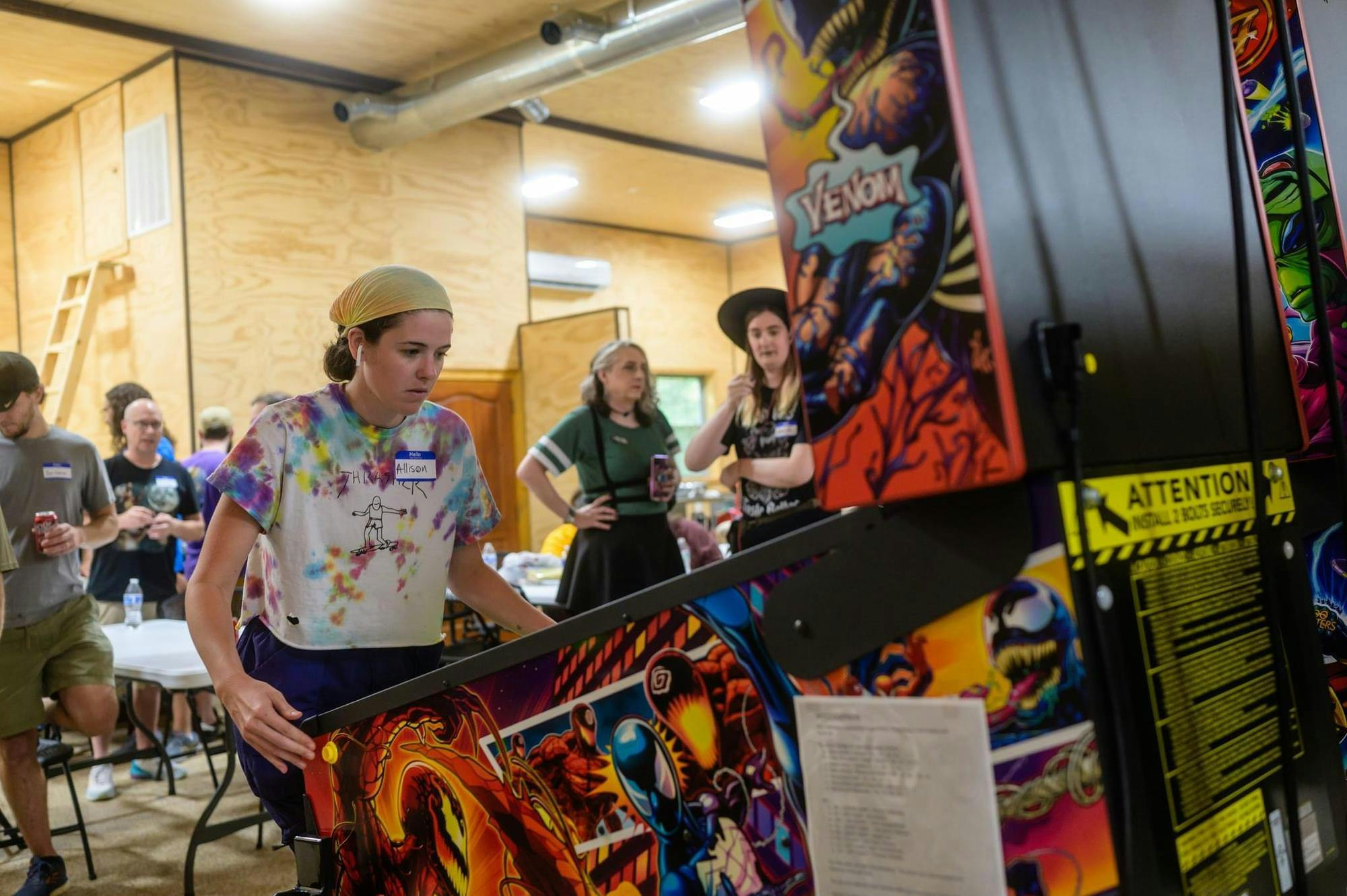 A woman plays at a pinball machine with the design of the Spider-Man villain Venom. Each machine is branded with many different intellectual properties ranging from movie franchises to popular characters.