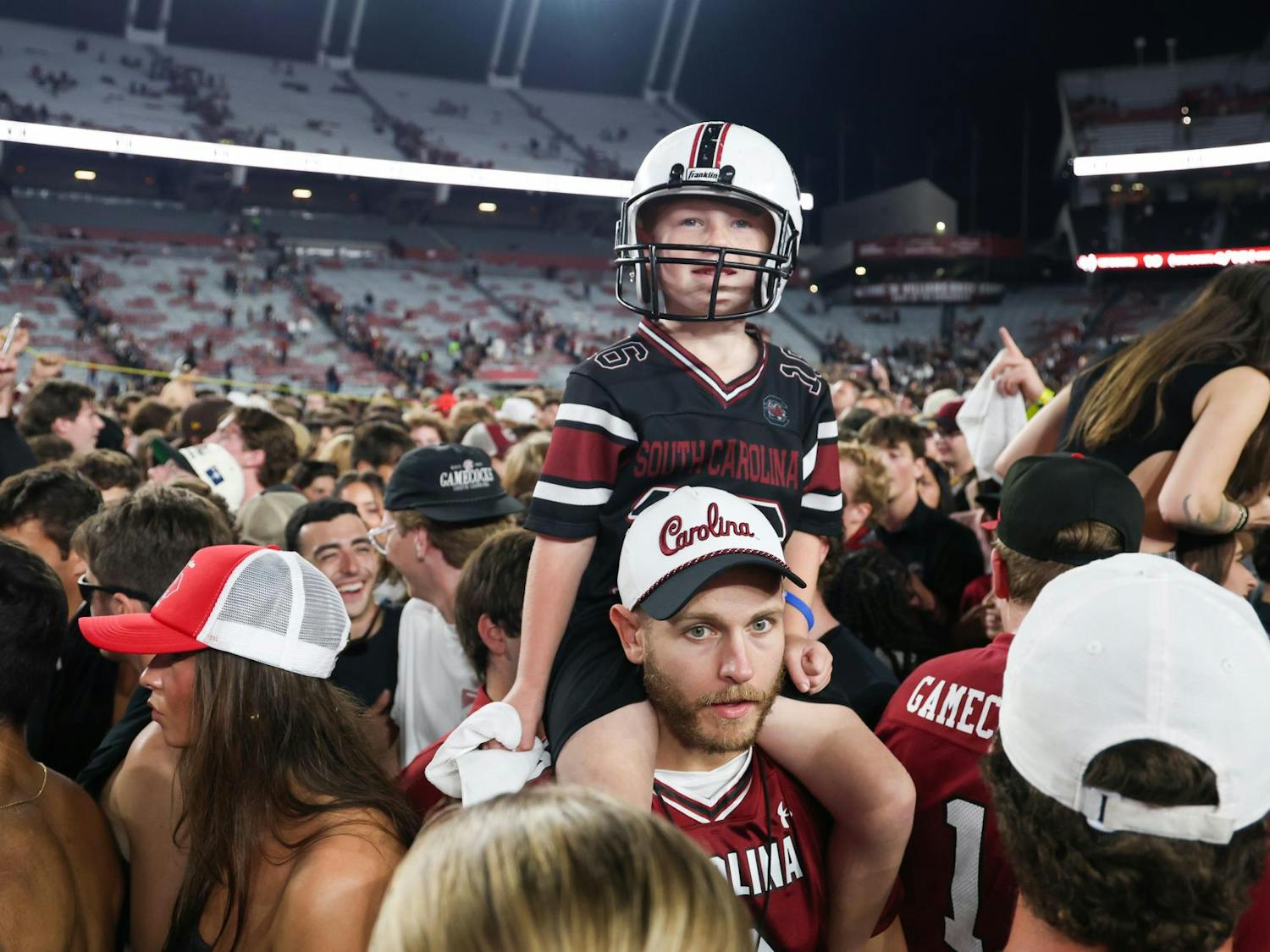 A young South Carolina fan sits on a man's shoulders in a crowd of people on the field at Williams-Brice Stadium on Nov. 2, 2024. South Carolina students and fans rushed the field after the team defeated No. 10 Texas A&M for the school's homecoming game.