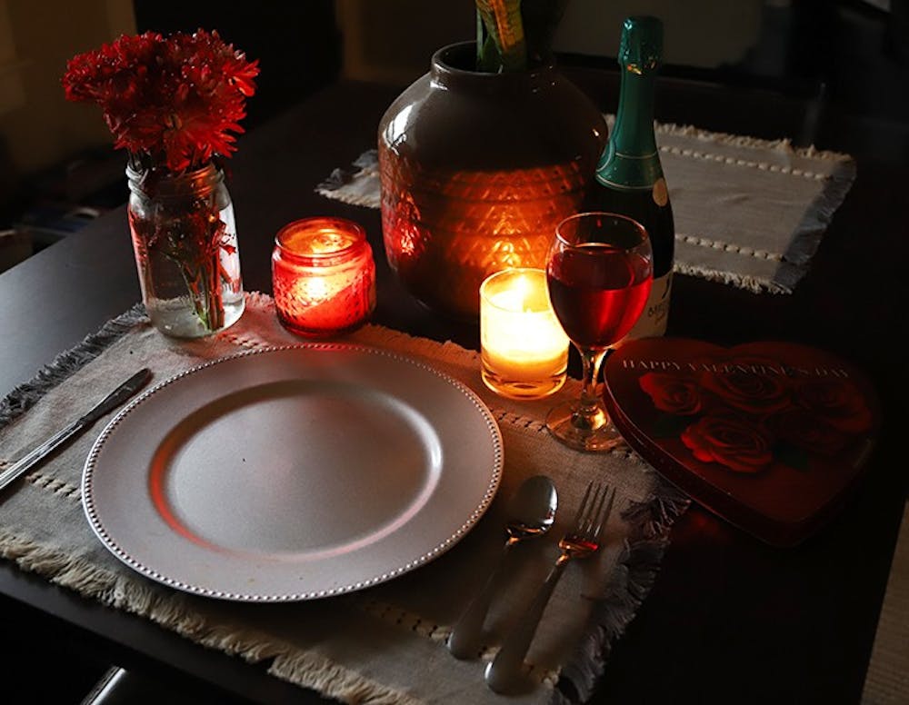 <p>A candle-lit table that is set for one with Valentine's Day paraphernalia surrounding the tableware.</p>