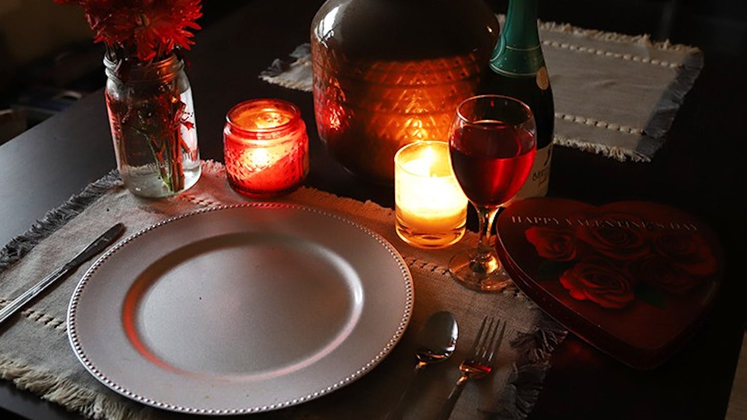 A candle-lit table that is set for one with Valentine's Day paraphernalia surrounding the tableware.