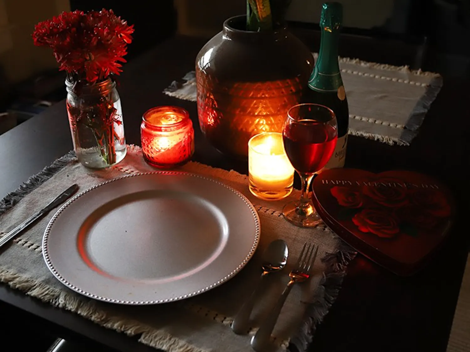 A candle-lit table that is set for one with Valentine's Day paraphernalia surrounding the tableware.
