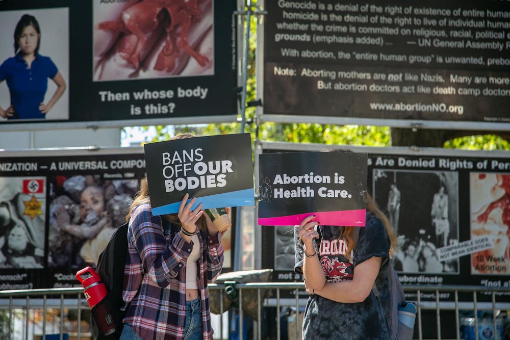 <p>Two protesters hide their faces from media during a counterprotest of the Genocide Awareness Project's display on the University of South Carolina campus on Oct. 22, 2024. Over the course of two days, the display was set up on Greene Street and Davis Field next to the Russell House Student Union.</p>