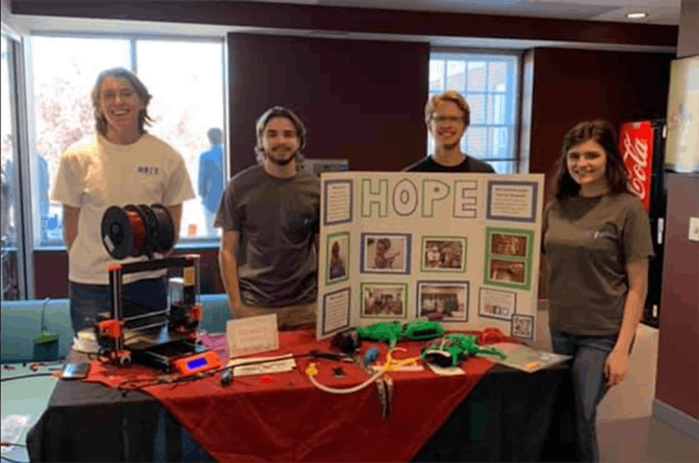<p>The Hands On Prosthetic Engineering organization at a table in the School of Journalism and Mass Communications. The table has an informational board, a 3D printer and examples of the organization's work.</p>