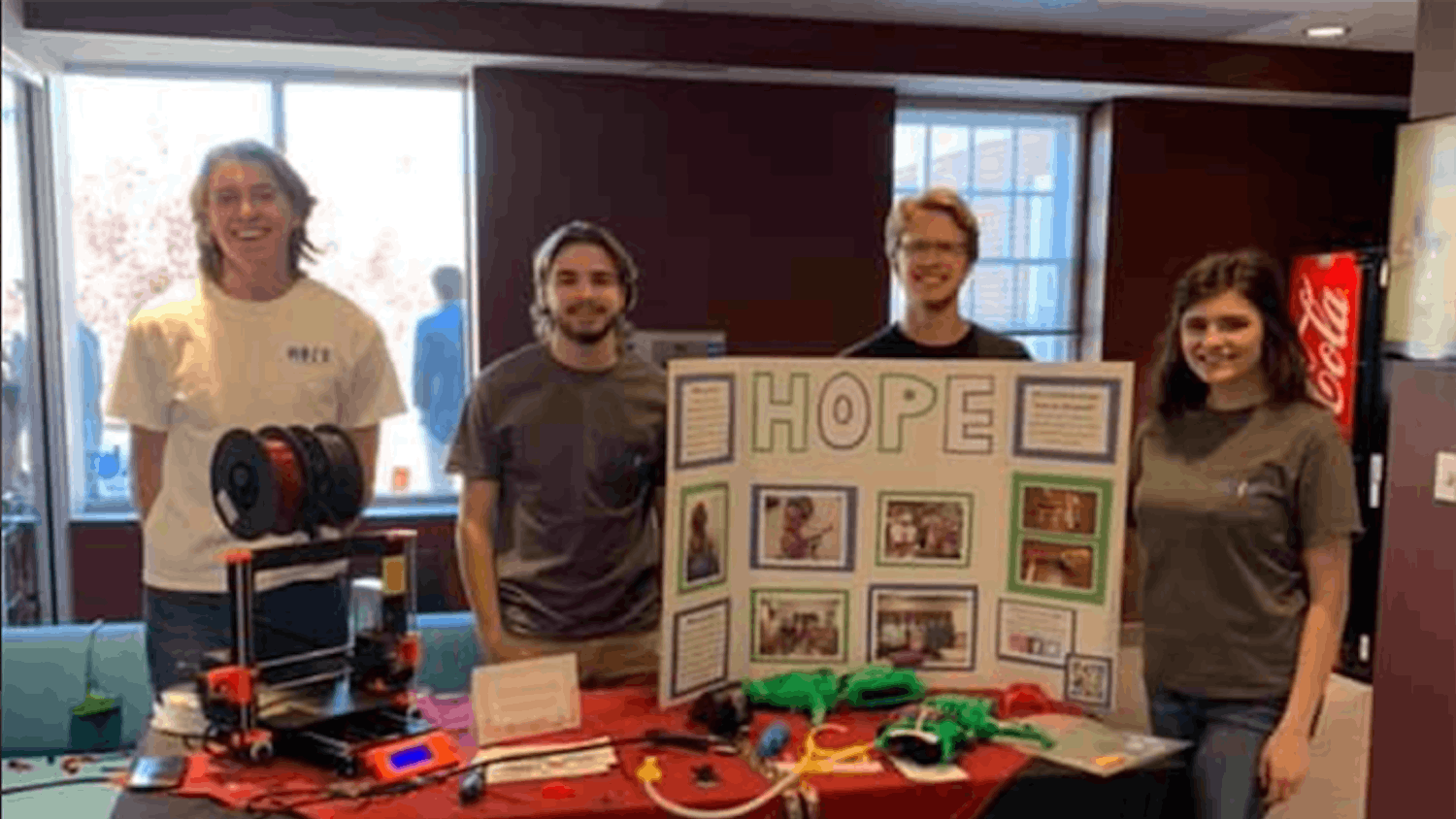 The Hands On Prosthetic Engineering organization at a table in the School of Journalism and Mass Communications. The table has an informational board, a 3D printer and examples of the organization's work.