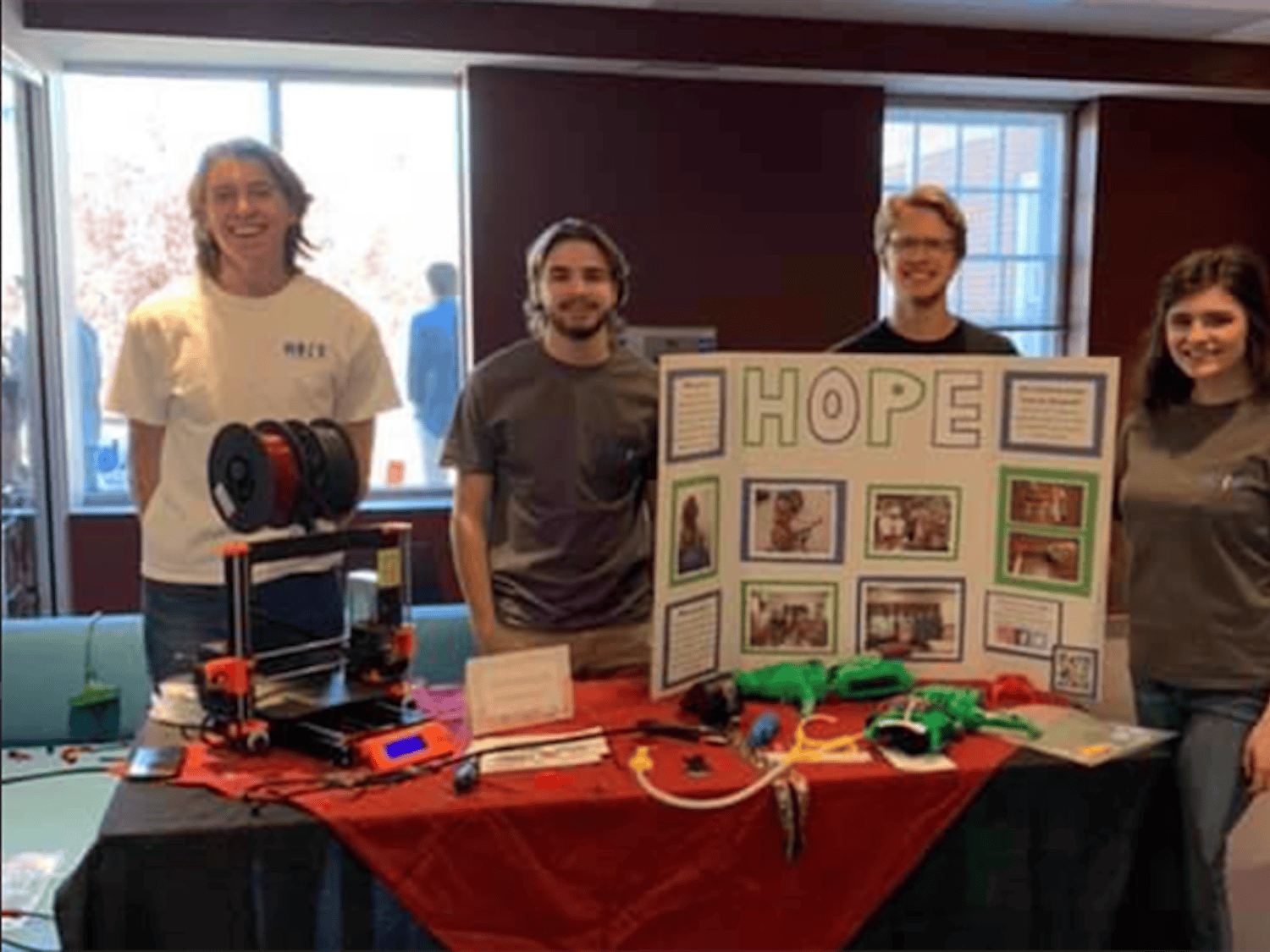 The Hands On Prosthetic Engineering organization at a table in the School of Journalism and Mass Communications. The table has an informational board, a 3D printer and examples of the organization's work.
