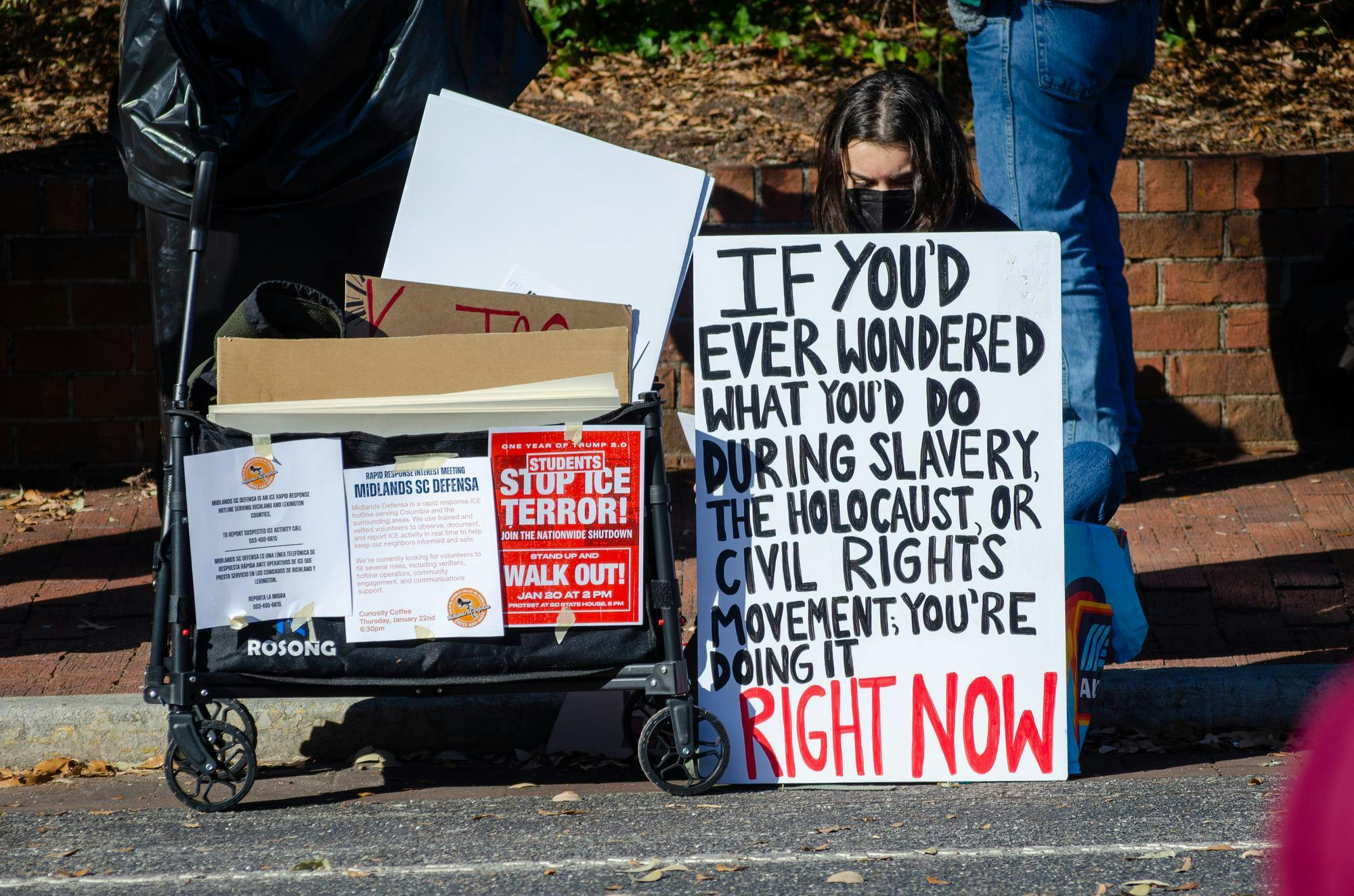 A student sits with a sign at a protest on Greene Street outside the Russell House in Columbia, South Carolina, on Jan. 20, 2026. Students walked out of their classes at 2 p.m. to protest the Trump administration and its aggressive deportation efforts.