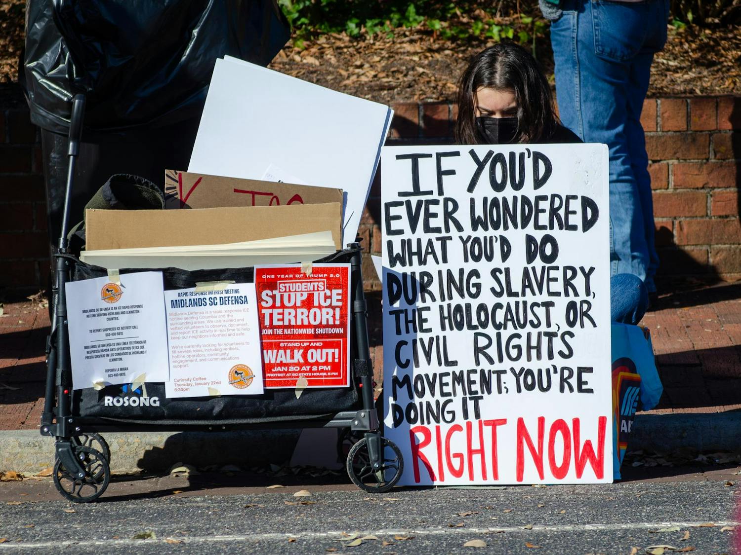A student sits with a sign at a protest on Greene Street outside the Russell House in Columbia, South Carolina, on Jan. 20, 2026. Students walked out of their classes at 2 p.m. to protest the Trump administration and its aggressive deportation efforts.