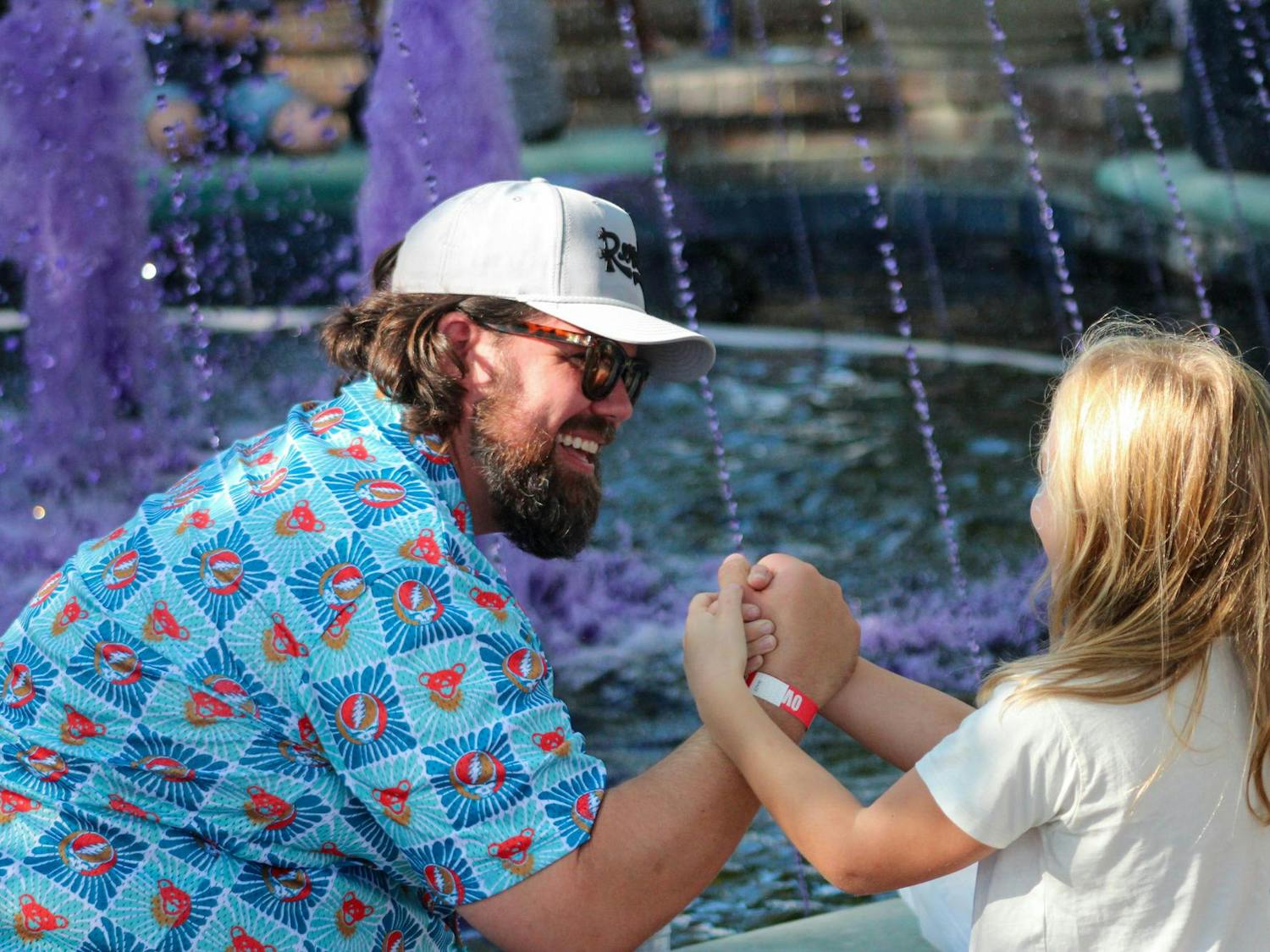 A father and daughter arm wrestle each other at the purple-dyed Five Points fountain during Jerryfest on Oct. 6, 2024. JerryFest, which was originally started by the owners of Loose Lucy’s, brought the annual festival to the Five Points Association back in 2014.