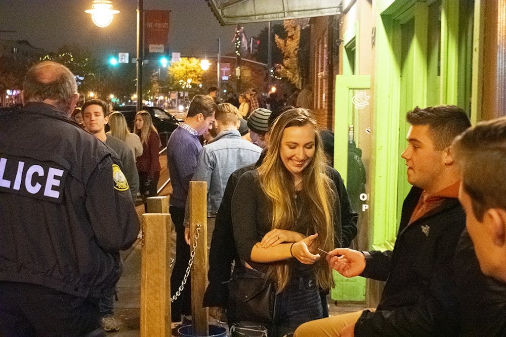 <p>A bouncer checks a student's ID outside Rooftop Bar. Everyone entering the bars in Five Points are required to show ID at the door. Bouncers often use scanners or lights to check the validity of IDs.</p>