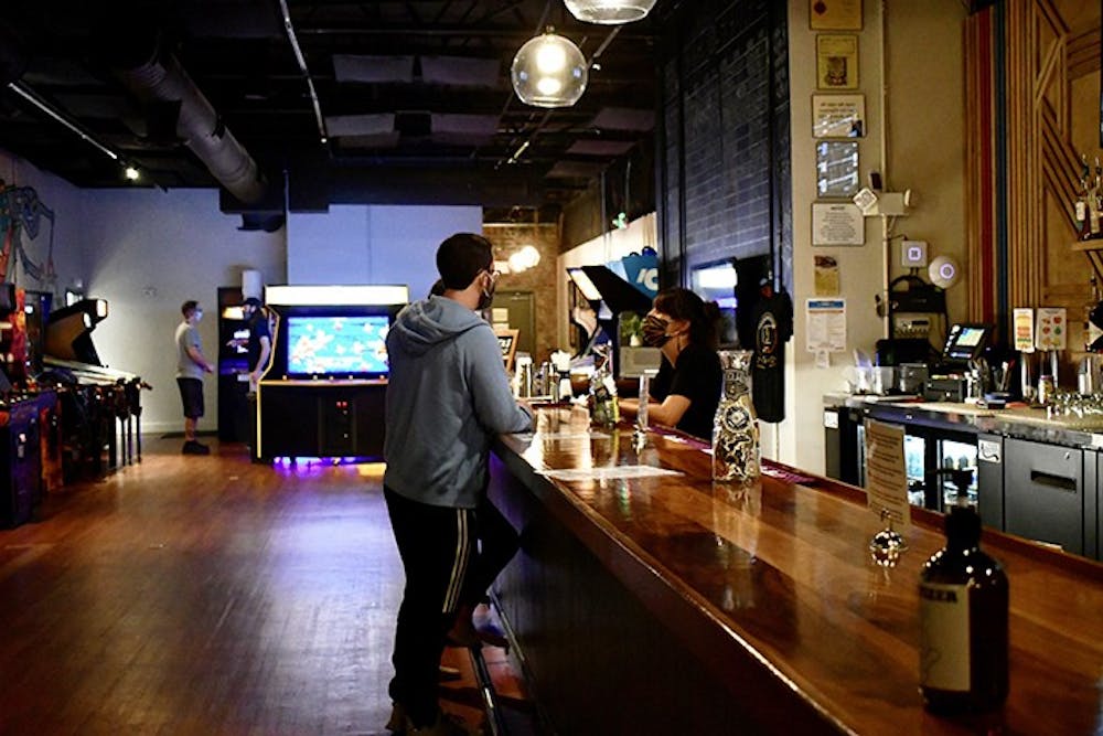 A customer orders from the bar in Transmission Arcade. The arcade is full of retro-themed games and artwork.