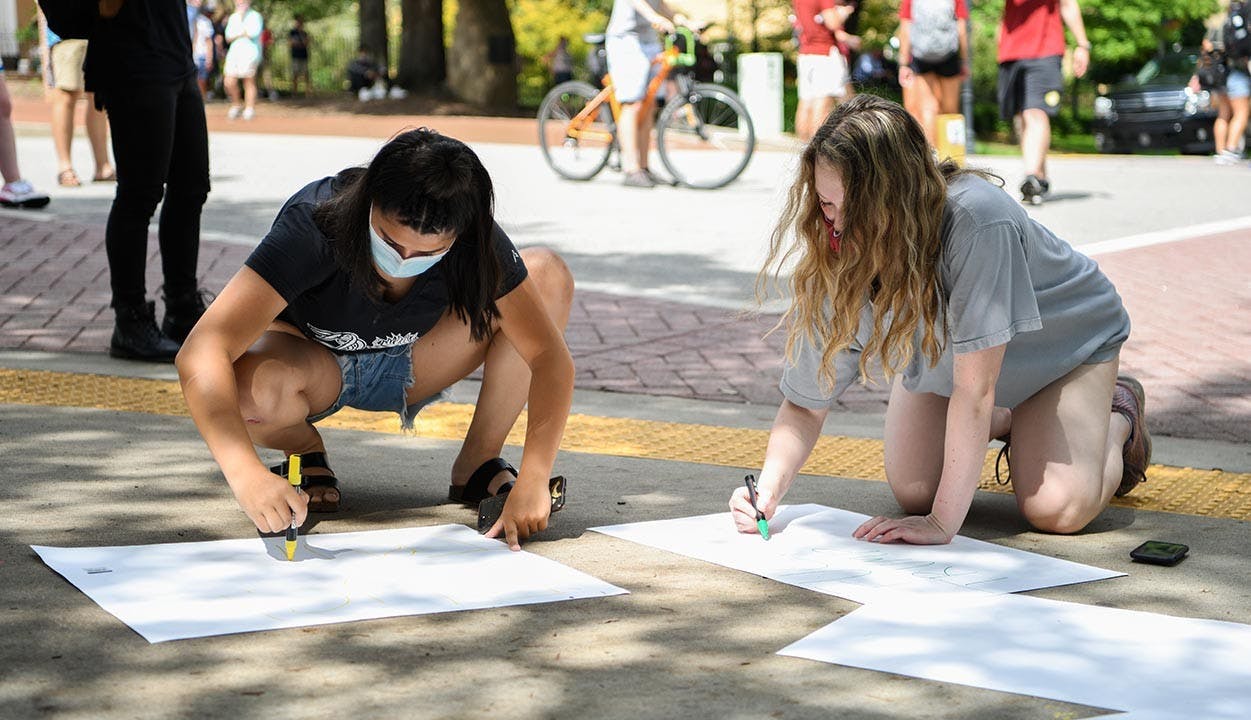 Two women make signs to protest Jim Gilles on Greene Street Friday. One person brought posters and markers and a group of students shared materials to create the signs.