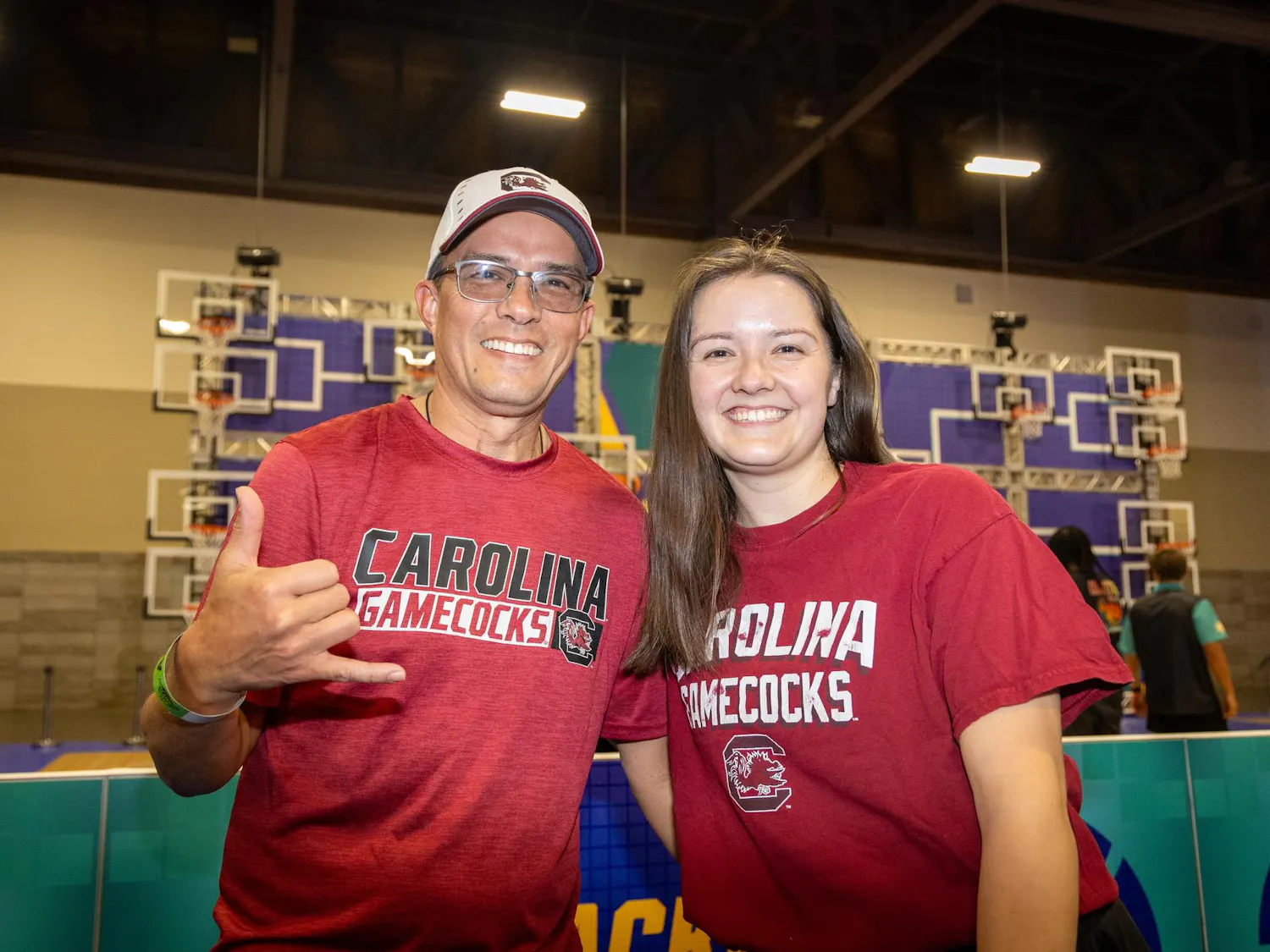 Phoenix, Arizona, resident Kevin Trechsel and Cincinnati, Ohio, resident Juliana Trechsel pose together in front of a basketball game at Tourney Town during March Madness in Phoenix on April 3, 2026. Juliana is a Gamecock alumna who came down to visit family in Phoenix, which Kevin said is a huge spot for all sporting events.