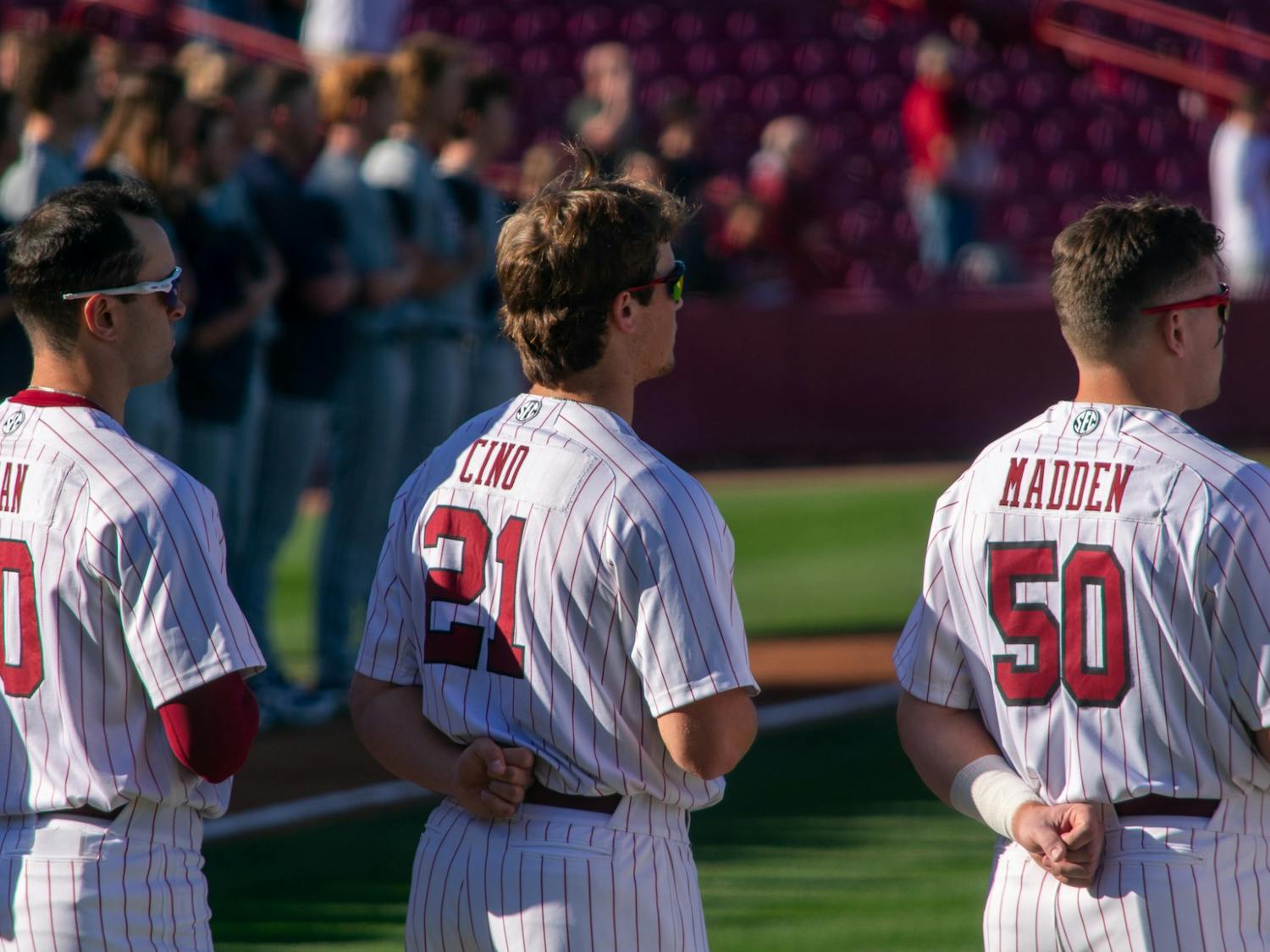 Carolina baseball team members Matt Hogan, Connor Cino, and Kevin Madden salute during the playing of the national anthem on Feb. 18, 2022. The Carolina Gamecocks won the first game in their series against UNCG 9-7.