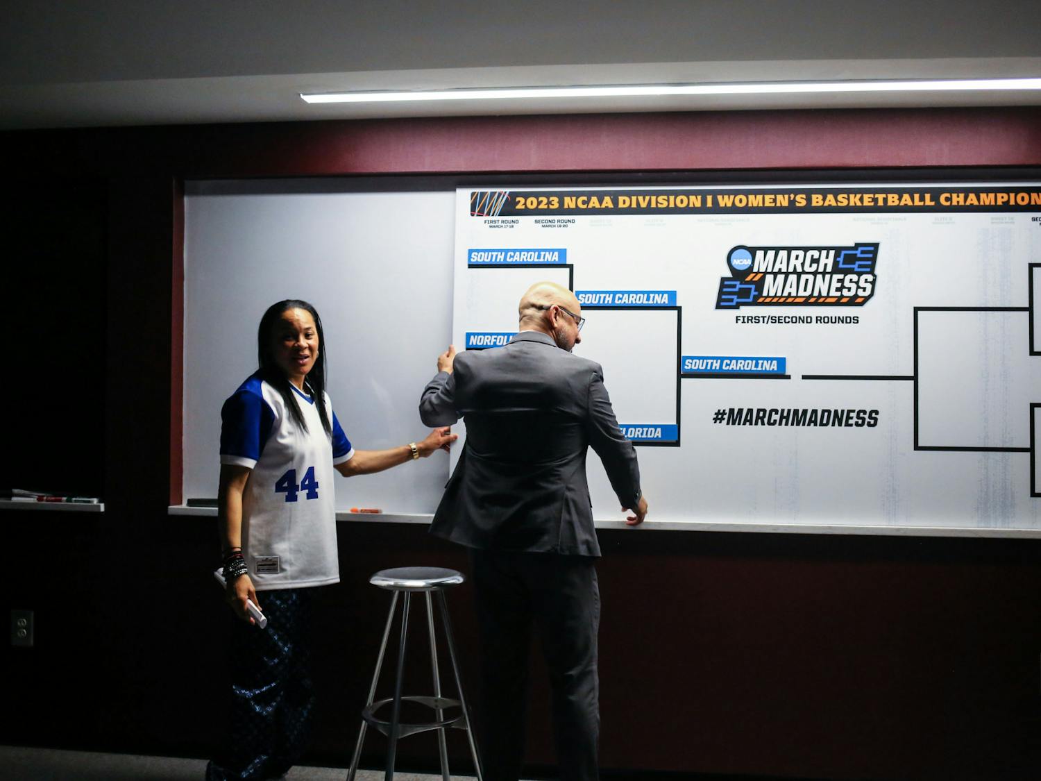 Head coach Dawn Staley and assistant coach Fred Chmiel hang an updated bracket in the South Carolina locker room following the team's second-round victory against South Florida in the NCAA tournament at Colonial Life Arena on March 19, 2023. The Gamecocks defeated the Bulls 76-45.